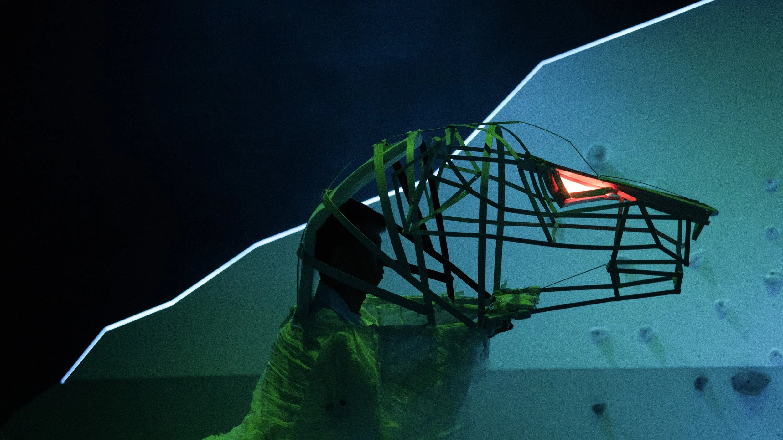 Close-up of performers climbing sculptural terrain in red lighting, contemporary set design by Ruby Law