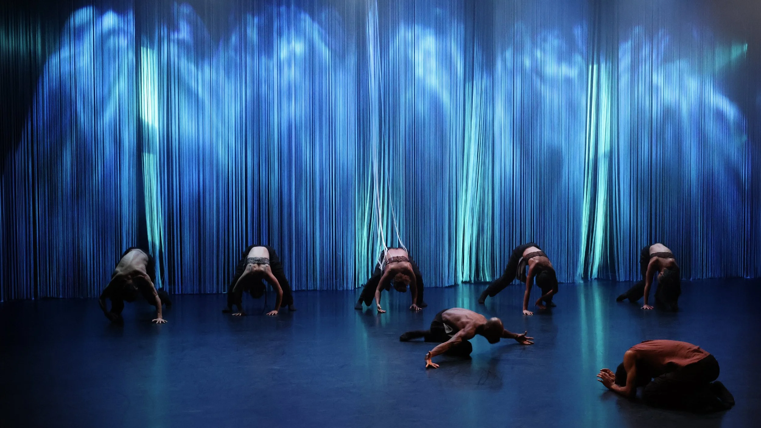 Projection mapping across cascading string curtain creating ethereal blue environment in Tellus by Dickson Mbi, stage design by London set designer Ruby Law.