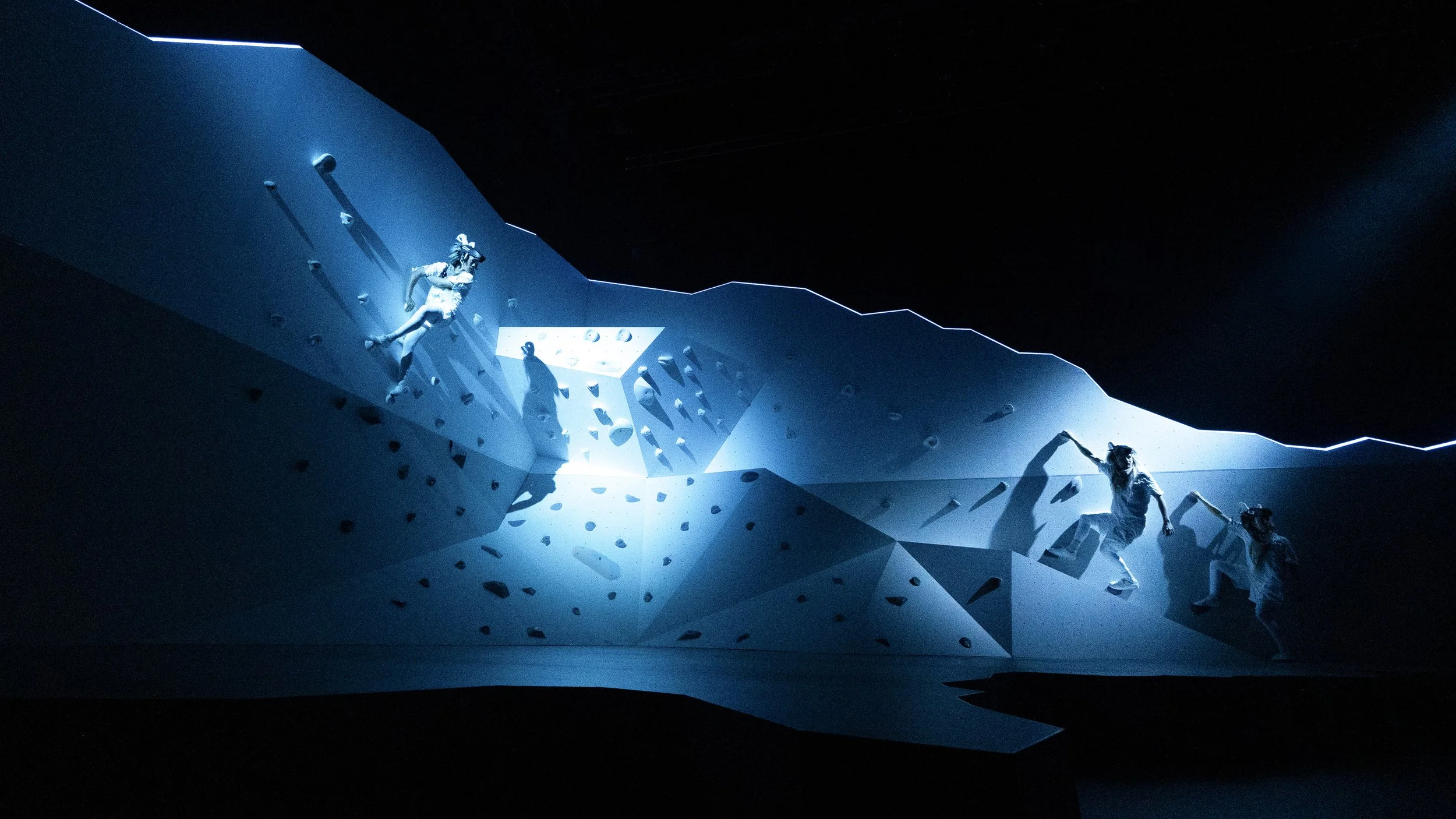 Performers climbing sculptural terrain under blue lighting, contemporary set design by Ruby Law RULA