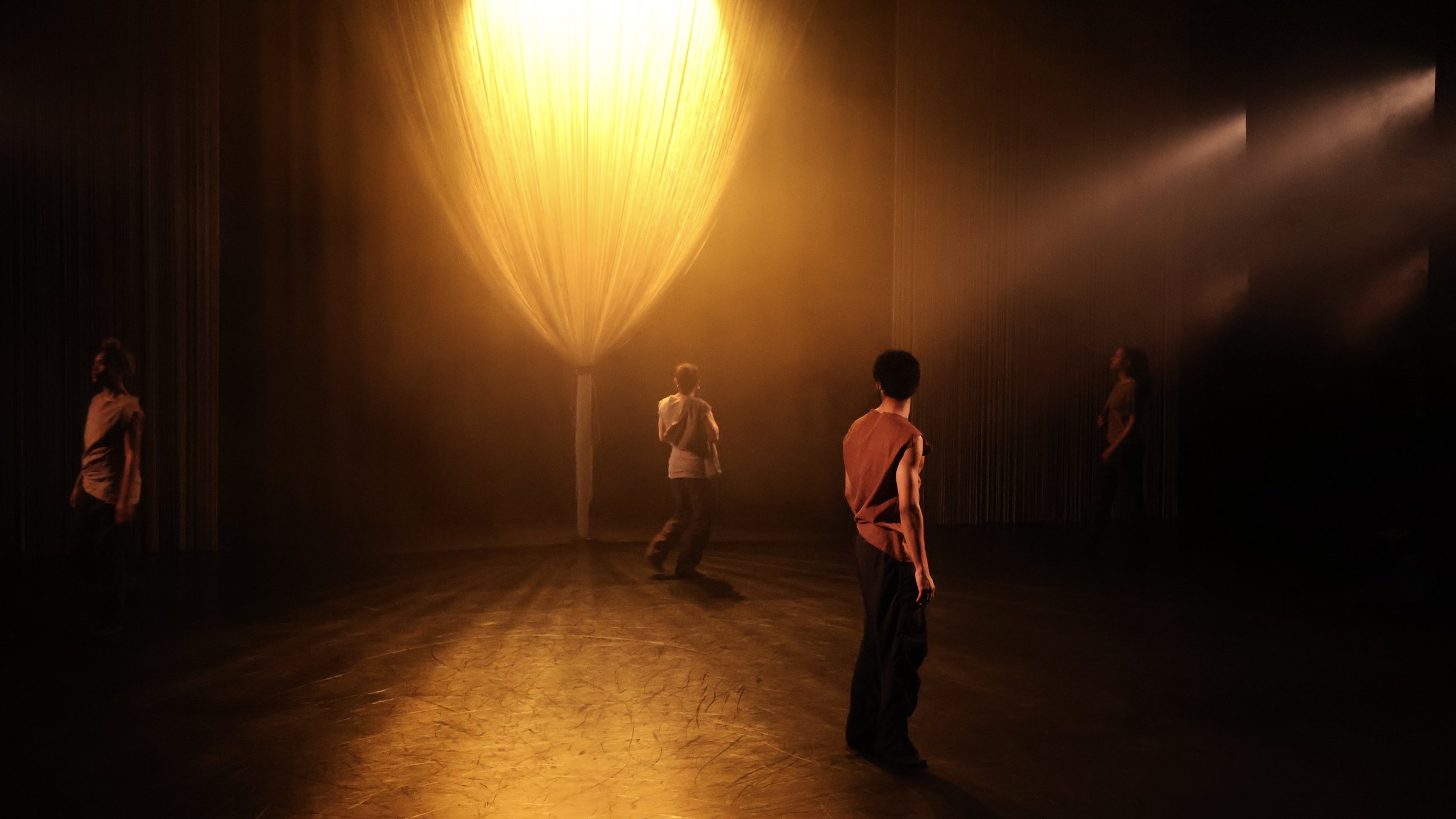 Dancers moving beneath glowing tree-like string curtain installation in Tellus by Dickson Mbi, contemporary dance set design by London stage designer Ruby Law.