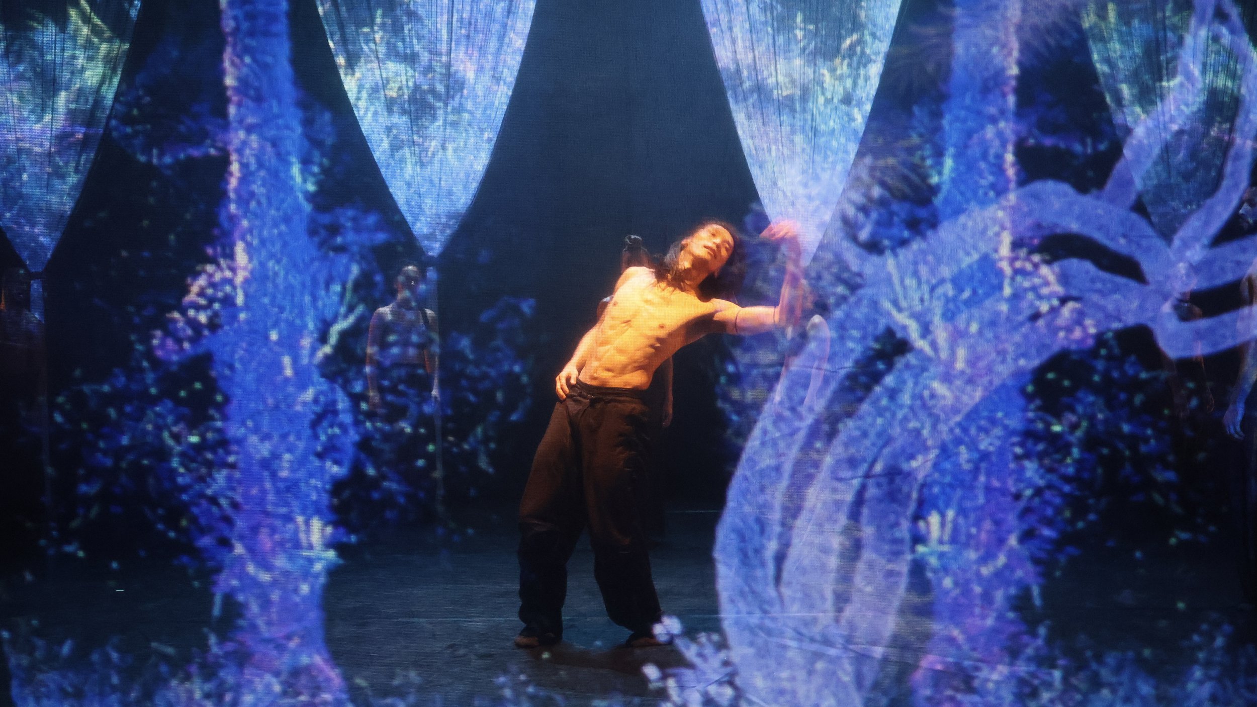 Solo performer framed by abstract digital foliage projections within string curtain installation in Tellus by Dickson Mbi, stage design by London designer Ruby Law.