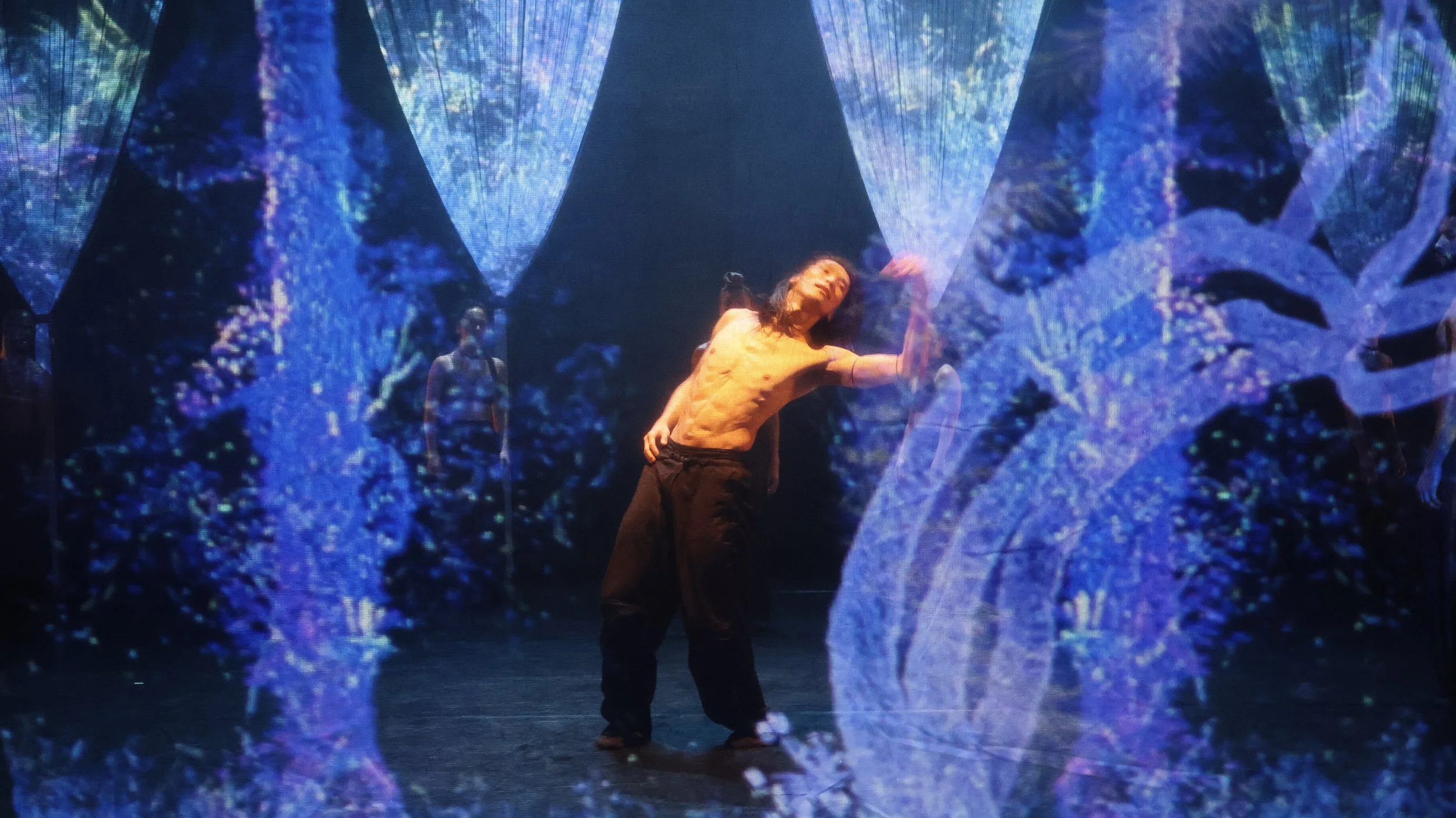 Solo performer framed by abstract digital foliage projections within string curtain installation in Tellus by Dickson Mbi, stage design by London designer Ruby Law.