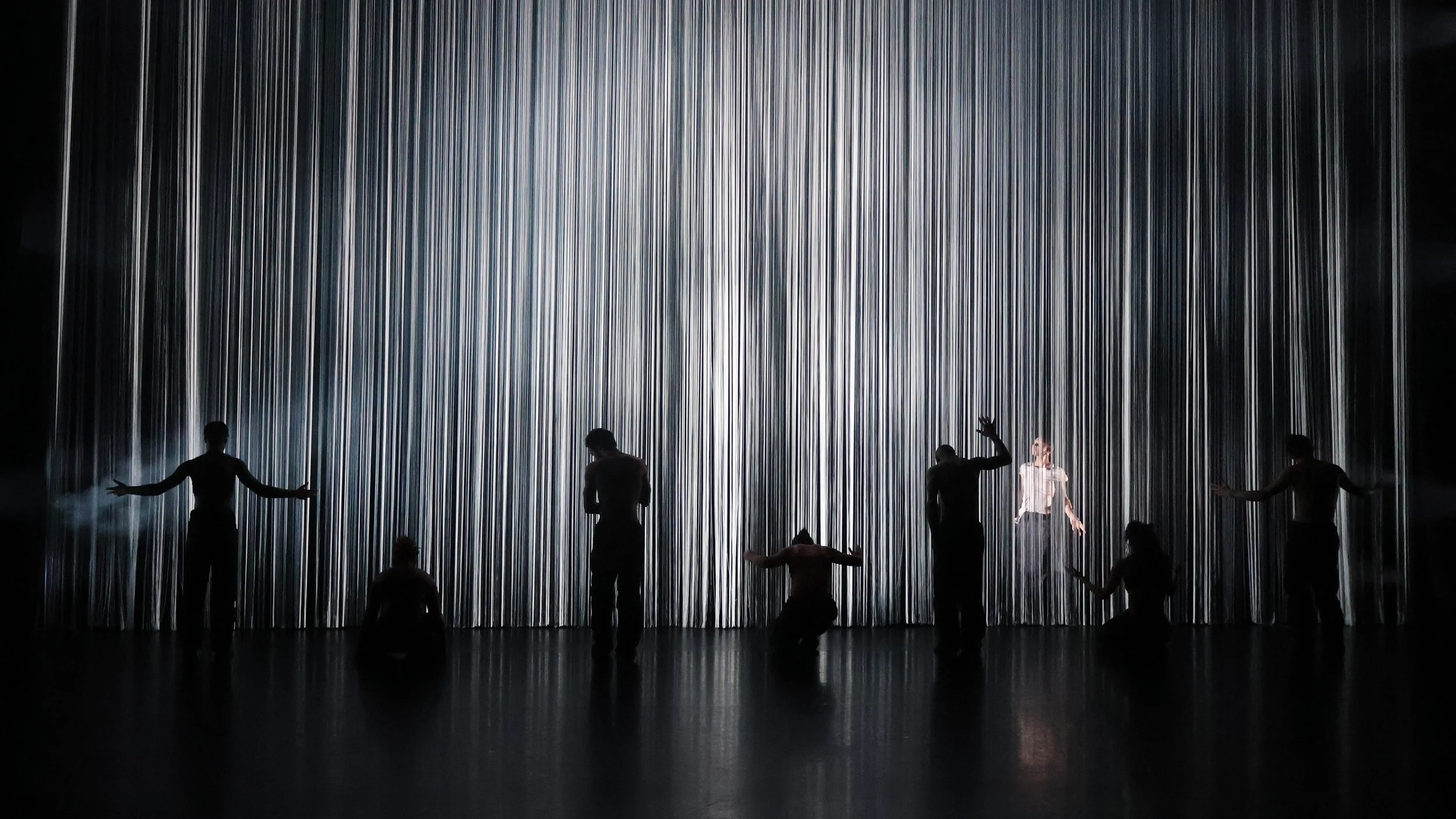 Silhouetted ensemble interacting with illuminated string curtain threshold in Tellus by Dickson Mbi, immersive dance set design by London designer Ruby Law.