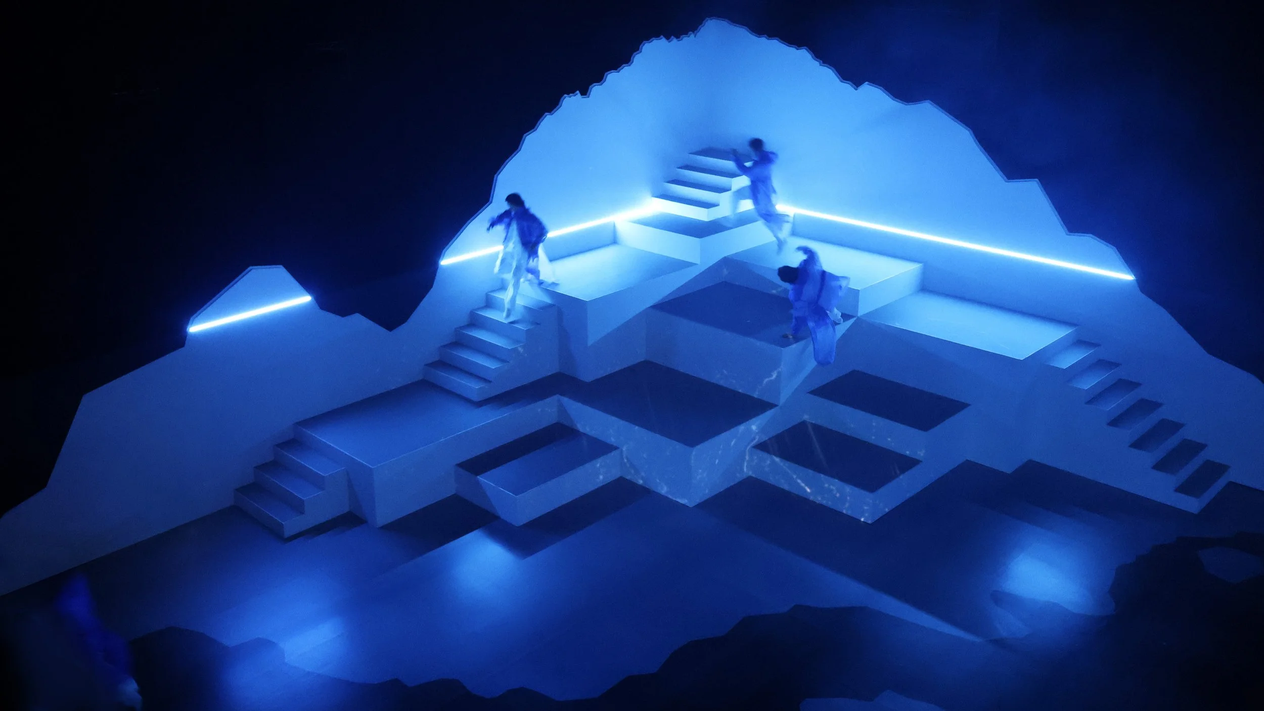 Multi-level stage with glowing lines and performers, immersive theatre design by Ruby Law of RULA London