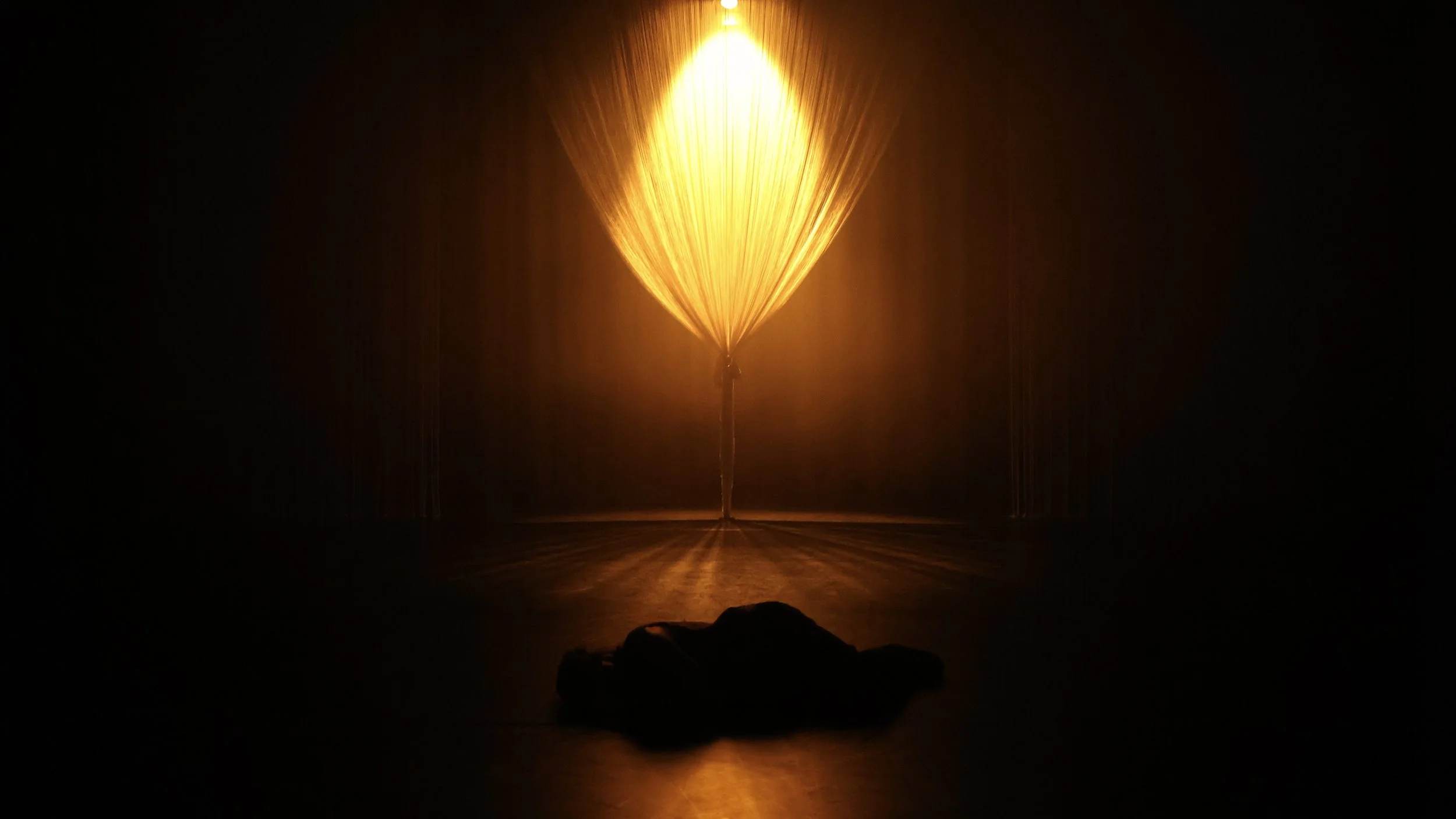 Golden light radiating through a string curtain forming an abstract tree in Tellus by Dickson Mbi, contemporary dance stage design by London set designer Ruby Law.