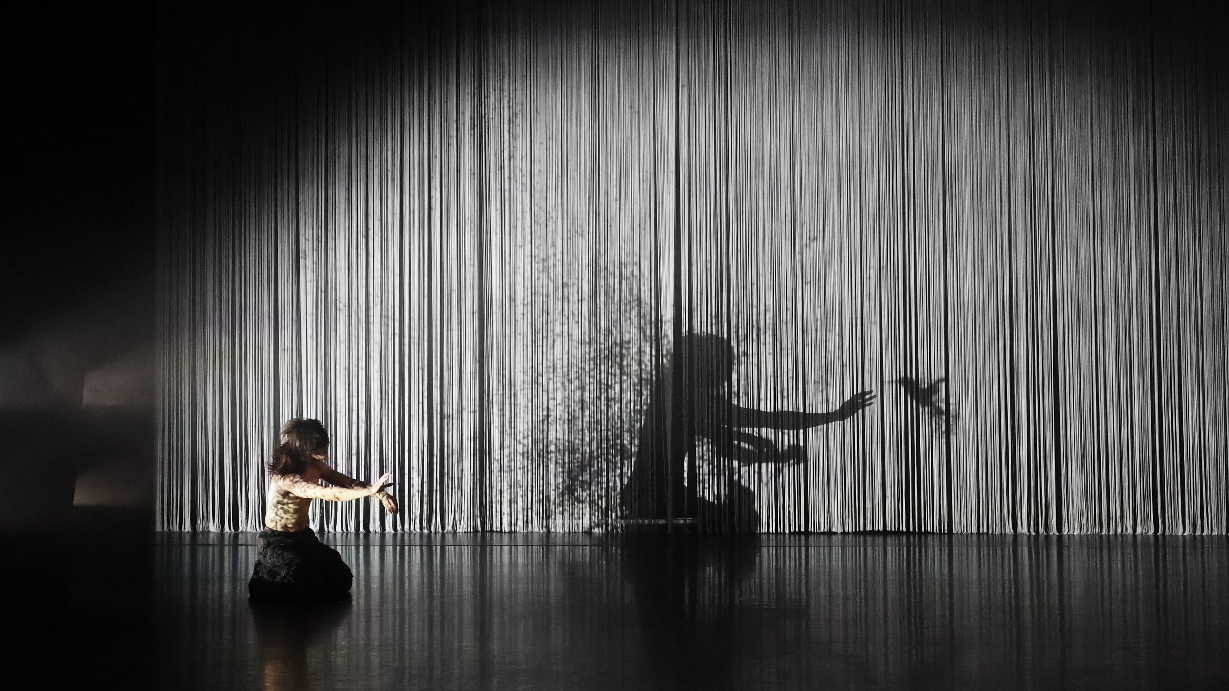 Performer interacting with textured string curtain creating fragmented shadow effect in Tellus by Dickson Mbi, immersive dance set design by London designer Ruby Law.