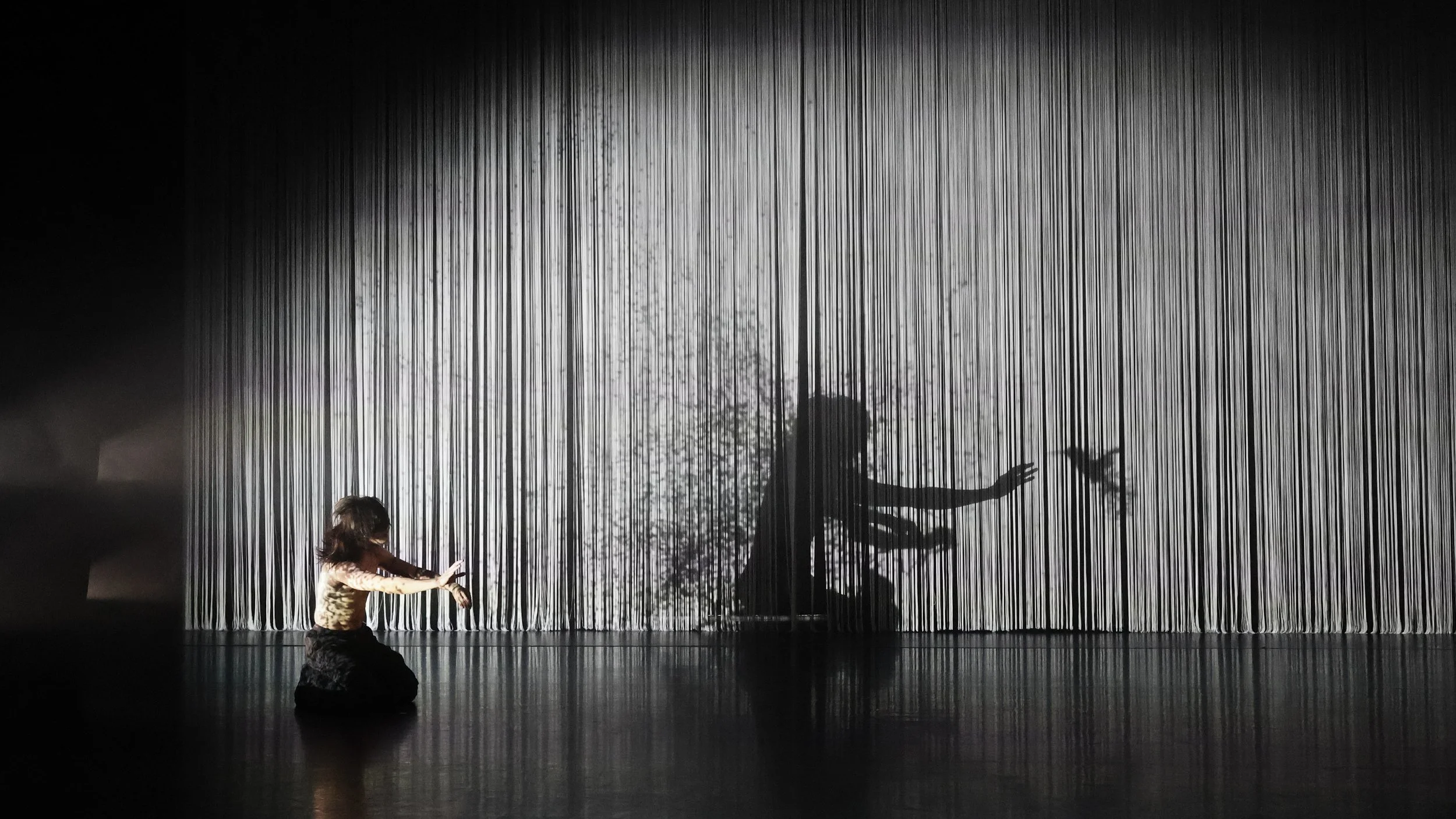 Performer interacting with textured string curtain creating fragmented shadow effect in Tellus by Dickson Mbi, immersive dance set design by London designer Ruby Law.