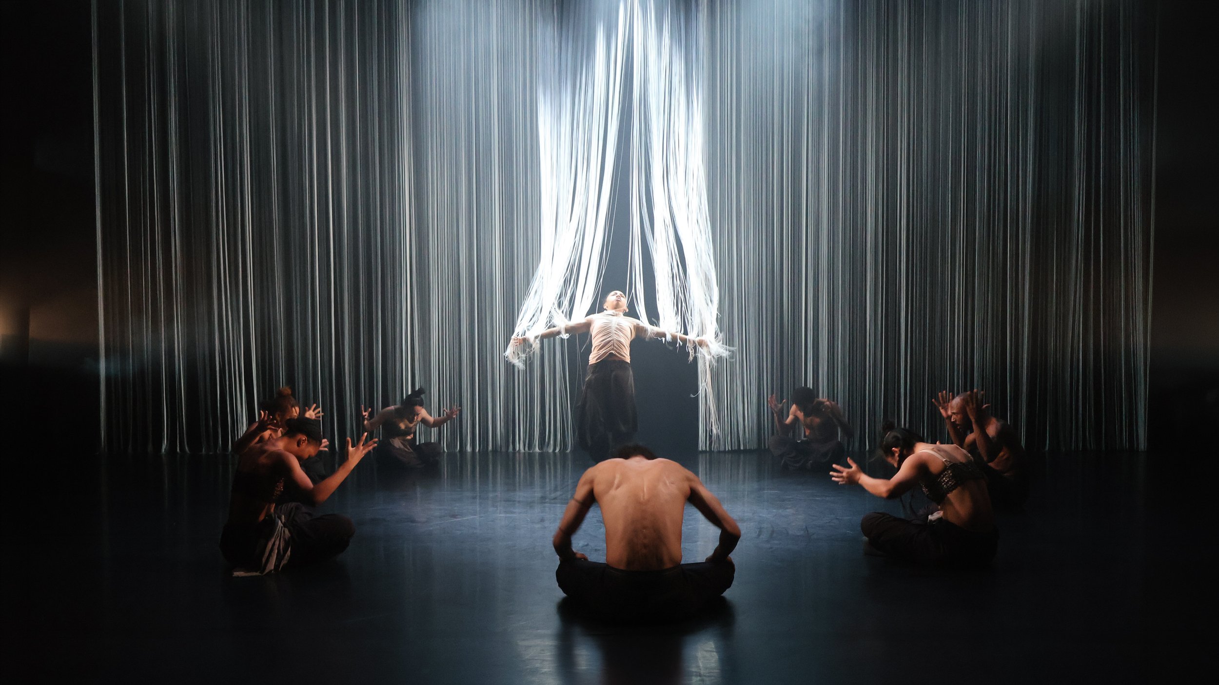 Central dancer lifted beneath cascading white string installation inspired by Mami Water in Tellus by Dickson Mbi, stage design by London set designer Ruby Law.