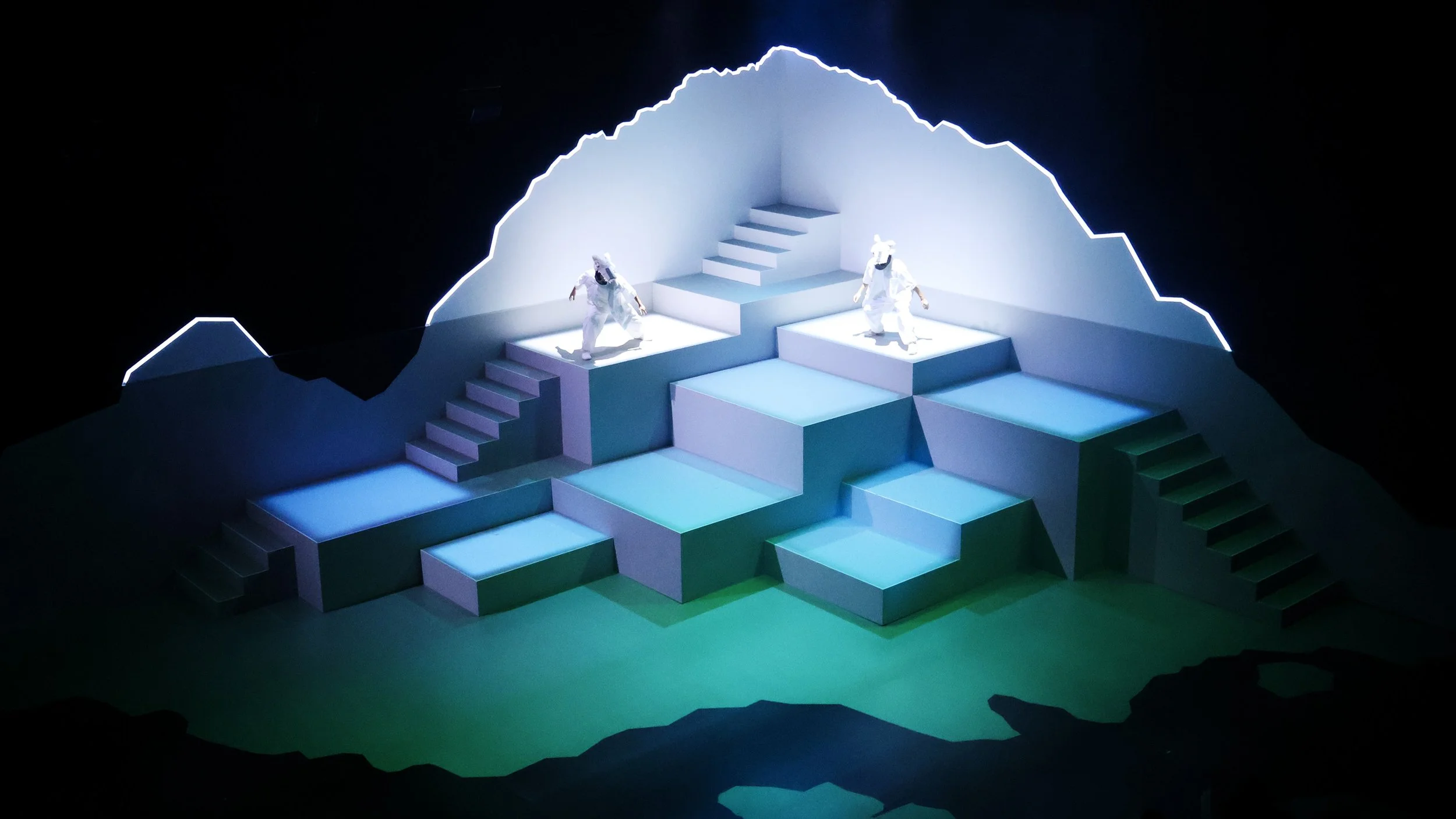 Tiered geometric mountain stage with performers, immersive theatre set design by Ruby Law RULA London