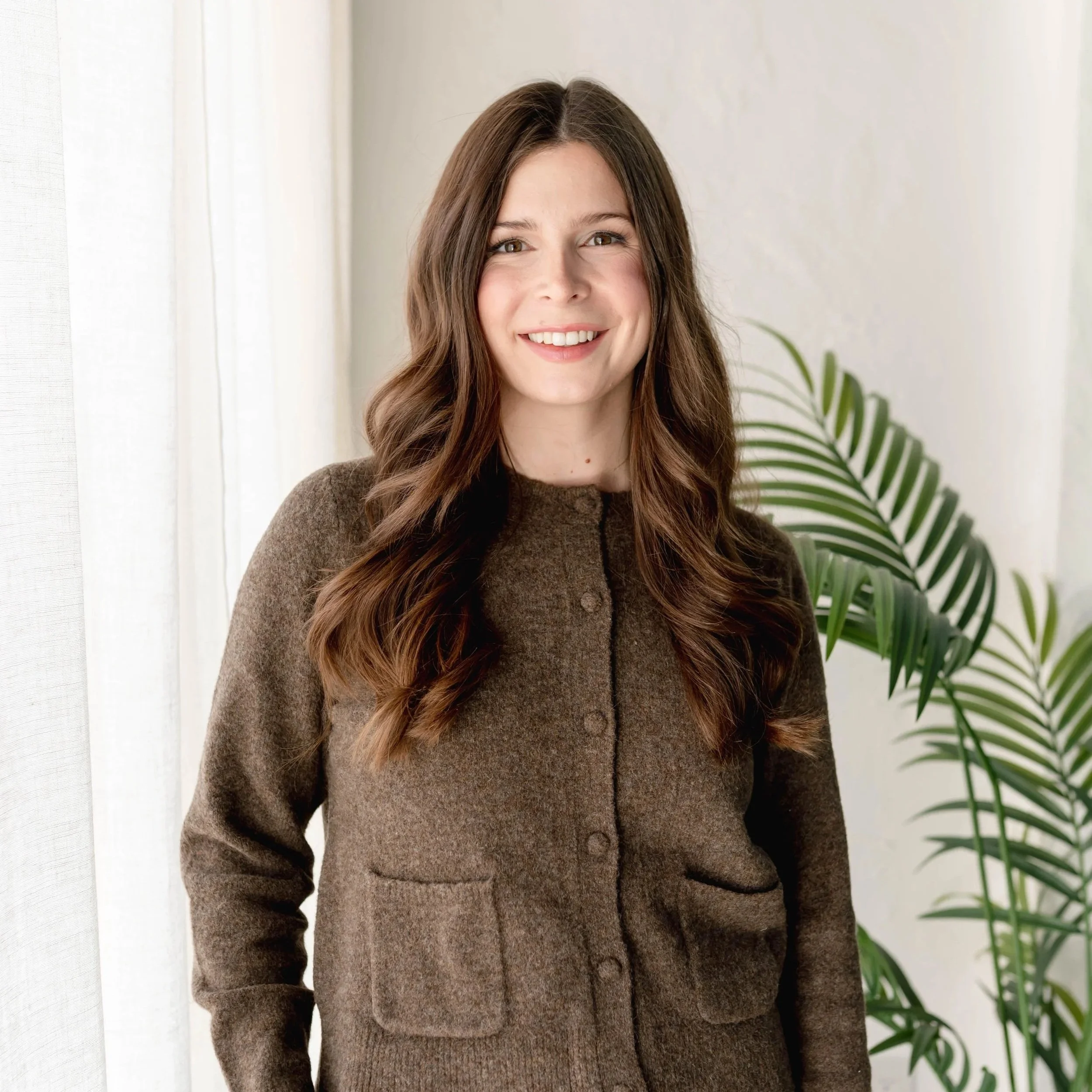 A woman with medium-length brown hair wearing a white sweater smiling on a neighborhood street.