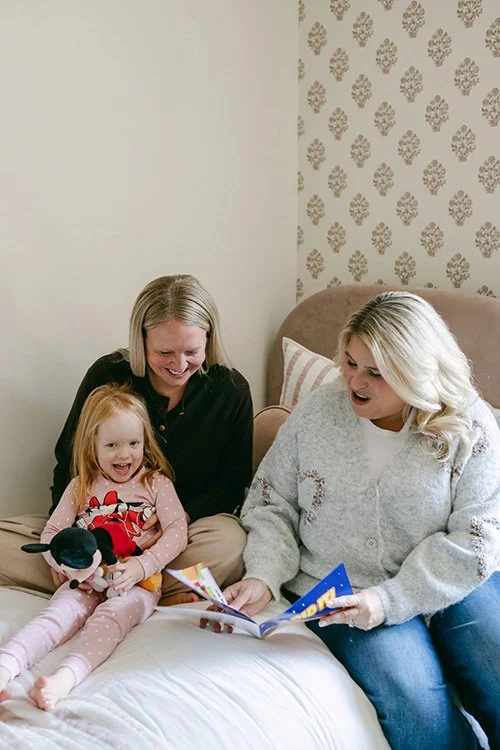 Sleep coach reading to mother and child on bed.