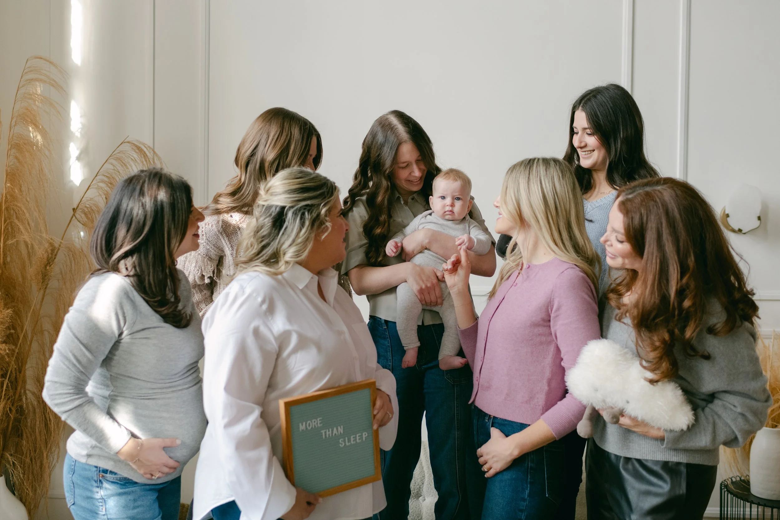 Group of women surrounding a baby, some smiling and others talking, in a cozy room with warm decor.