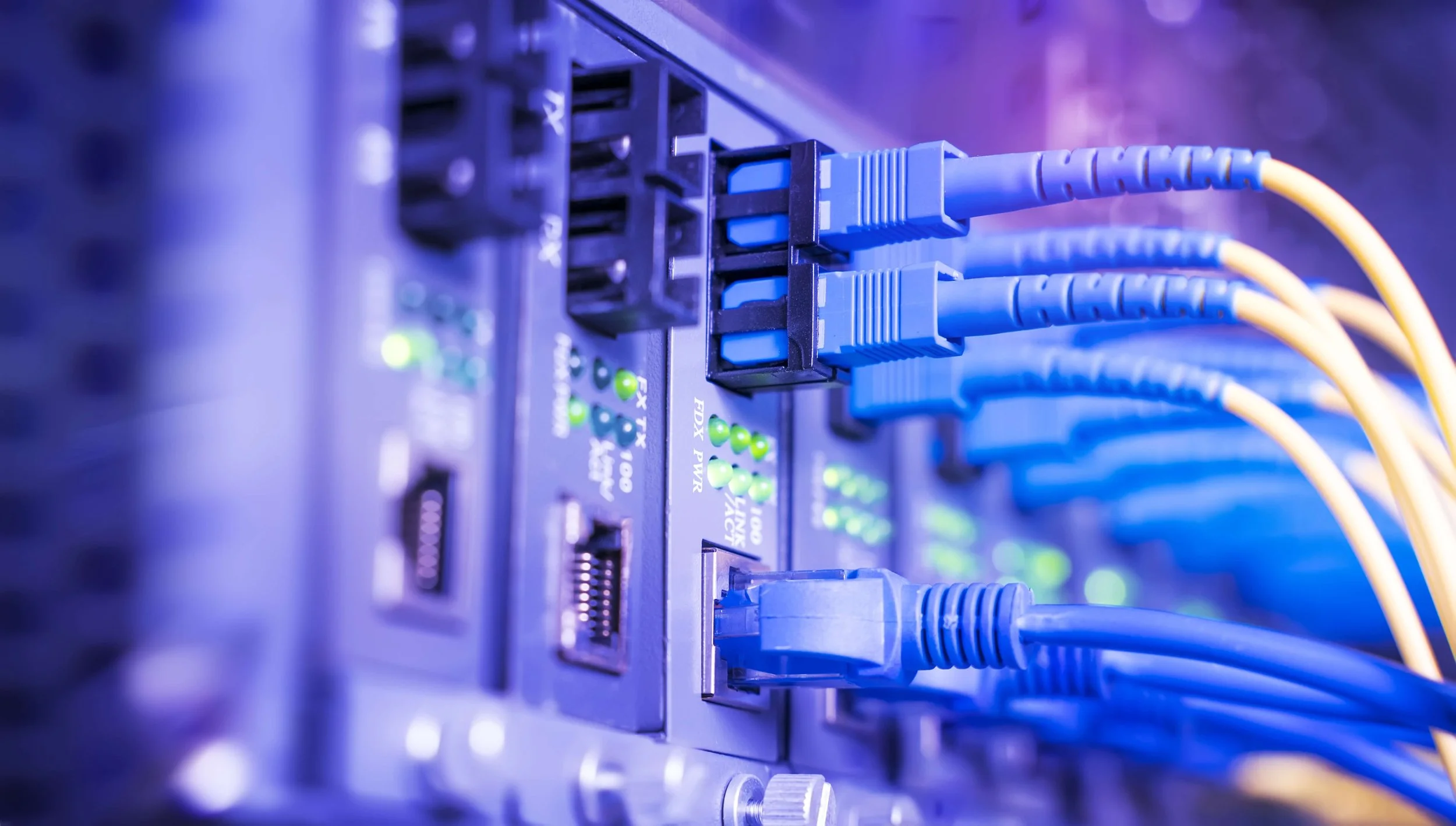 Close-up of a server rack with multiple Ethernet cables connected to network ports, illuminated by green LED indicator lights.