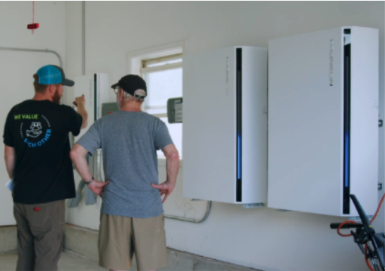 Earthlight technician standing next to a customer and pointing to FranklinWH batteries installed in his home