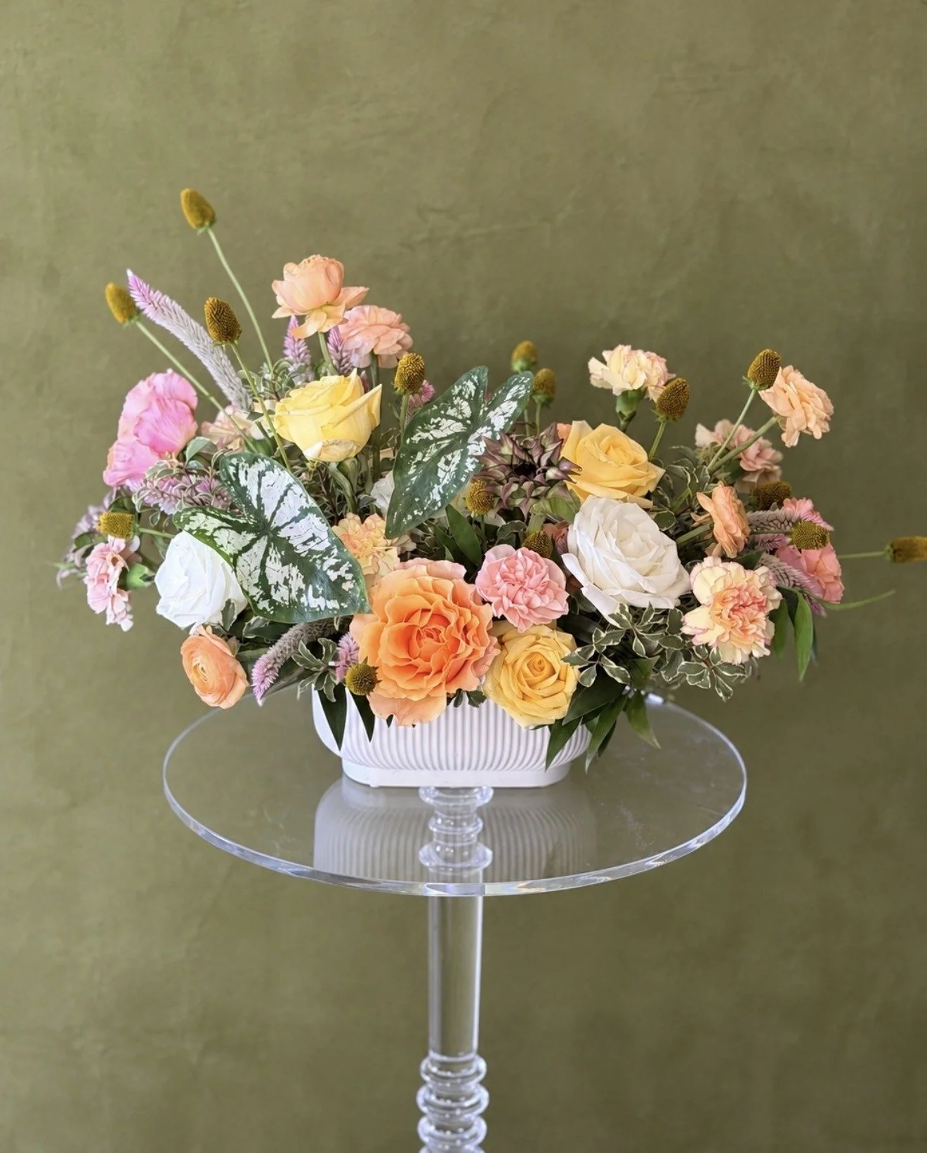 Pastel fall floral arrangement with peach, blush, pale yellow and white flowers, caladium leaves and seasonal greenery in a white vase.