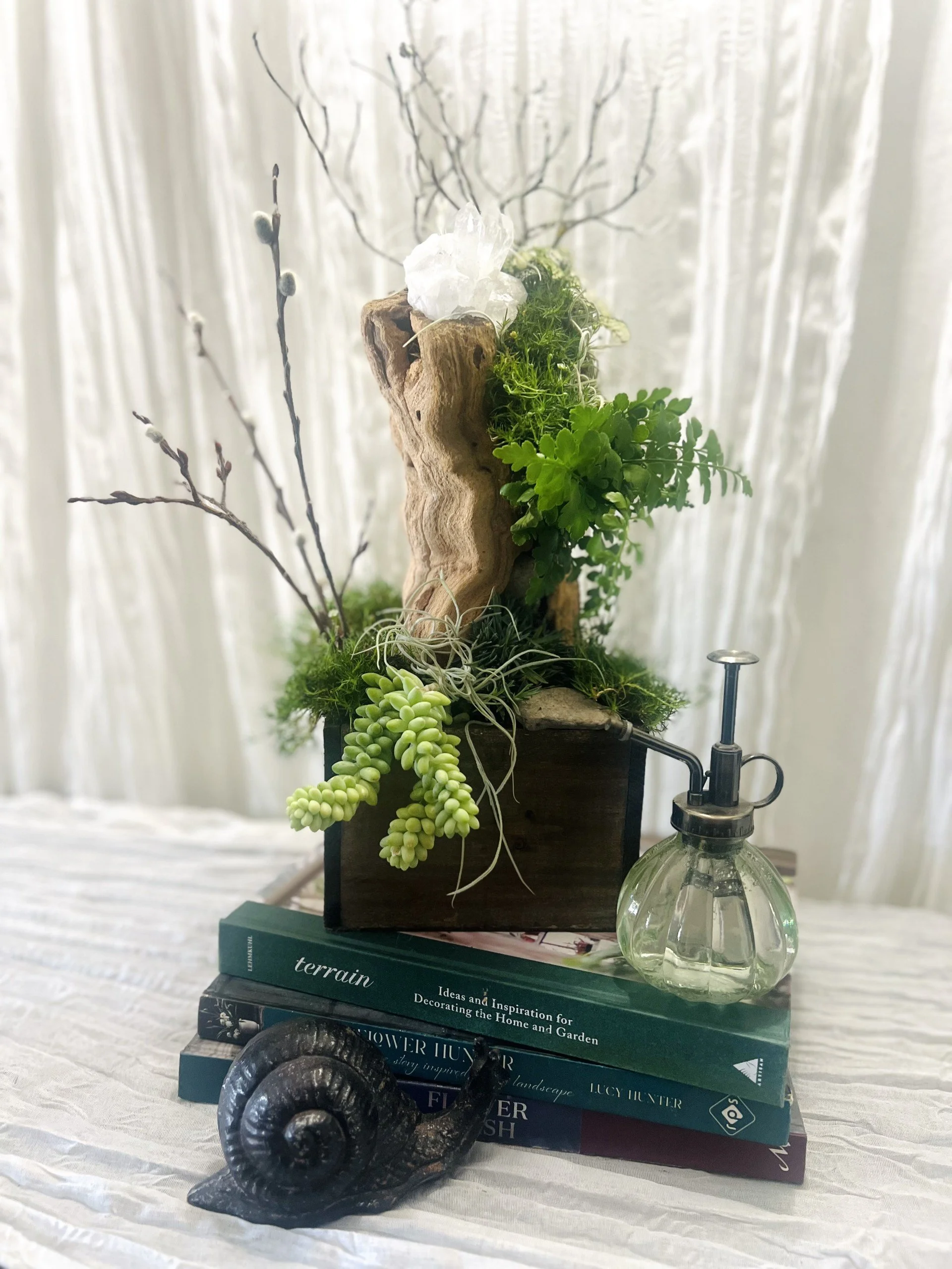 Luxury living desk garden displayed on an office desk featuring succulents, flowering grasses, driftwood, Spanish moss, polka dot plants, and natural amethyst crystals
