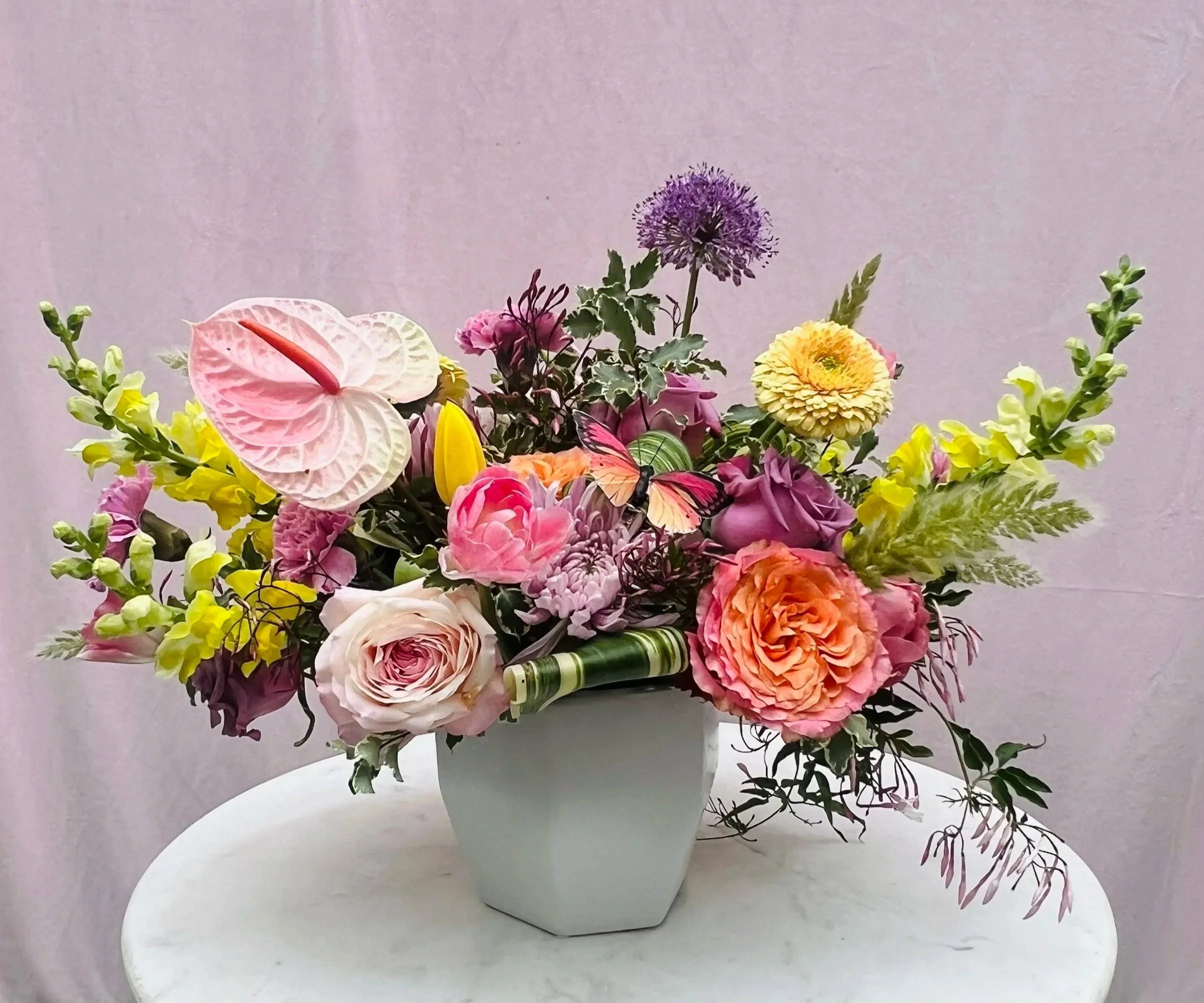 Luxury pastel flower arrangement designed with unique florals in shades of pink, yellow, orange, and lavender in a high end vase.