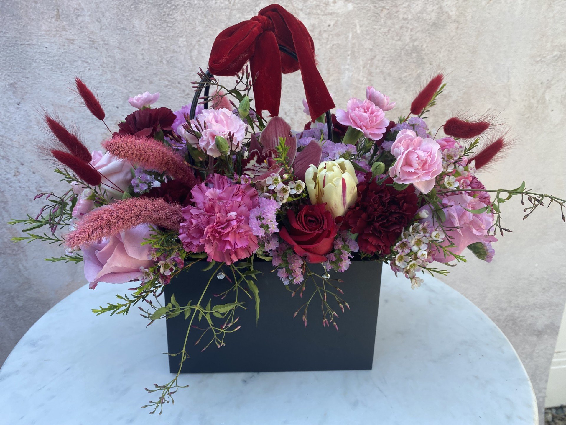 Luxury floral arrangement featuring premium seasonal flowers in deep red, burgundy, crimson, and rich pink designed in a reusable kraft keepsake tote bag