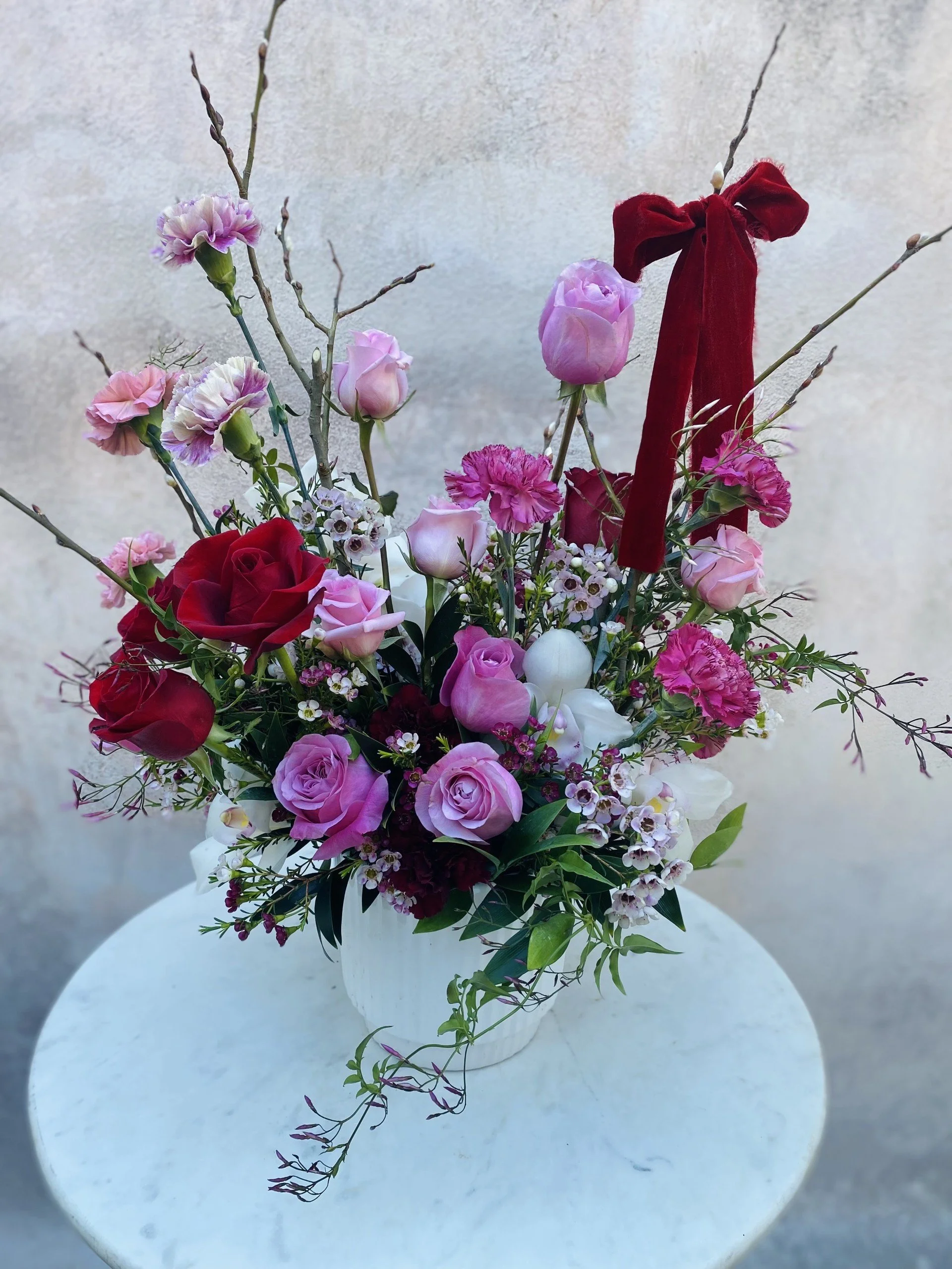 Romantic red, pink, and white orchid flower arrangement with seasonal blooms and lush greenery, back view showing full garden-style structure