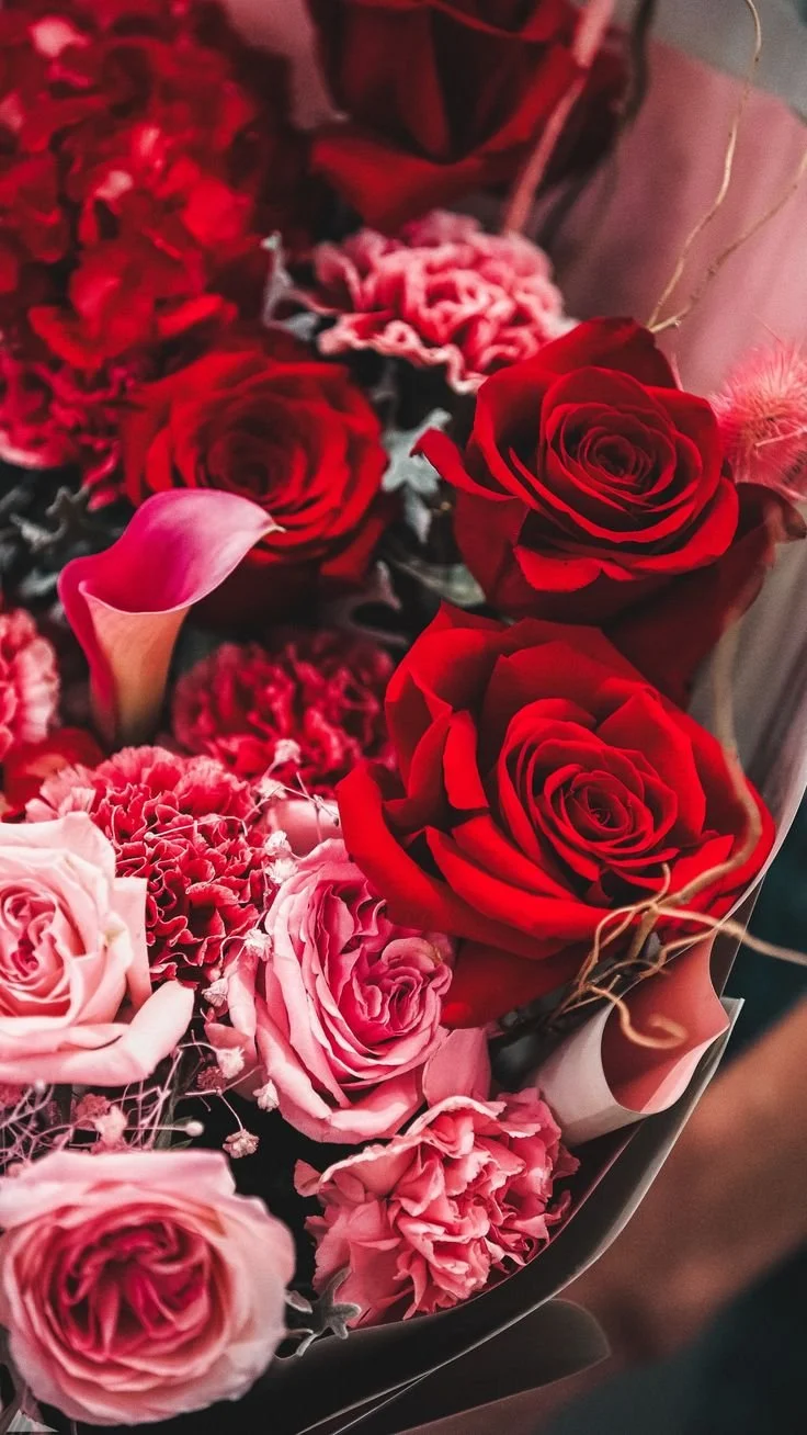 Close up of layered, textured florals and greenery in shades of deep red, burgundy, and dark pink