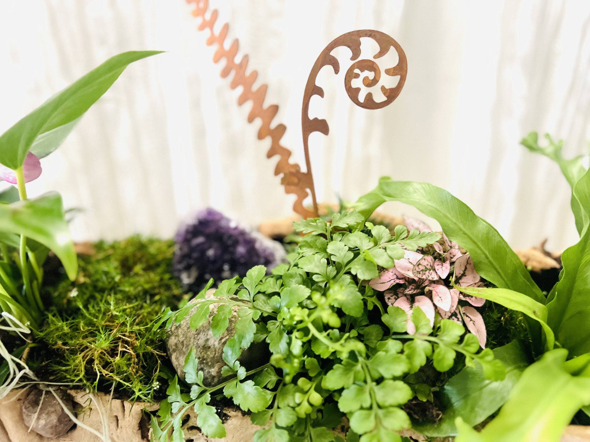 Decorative metal garden stakes surrounded by Spanish moss, blooming grasses, and living plants in a handcrafted driftwood desk planter
