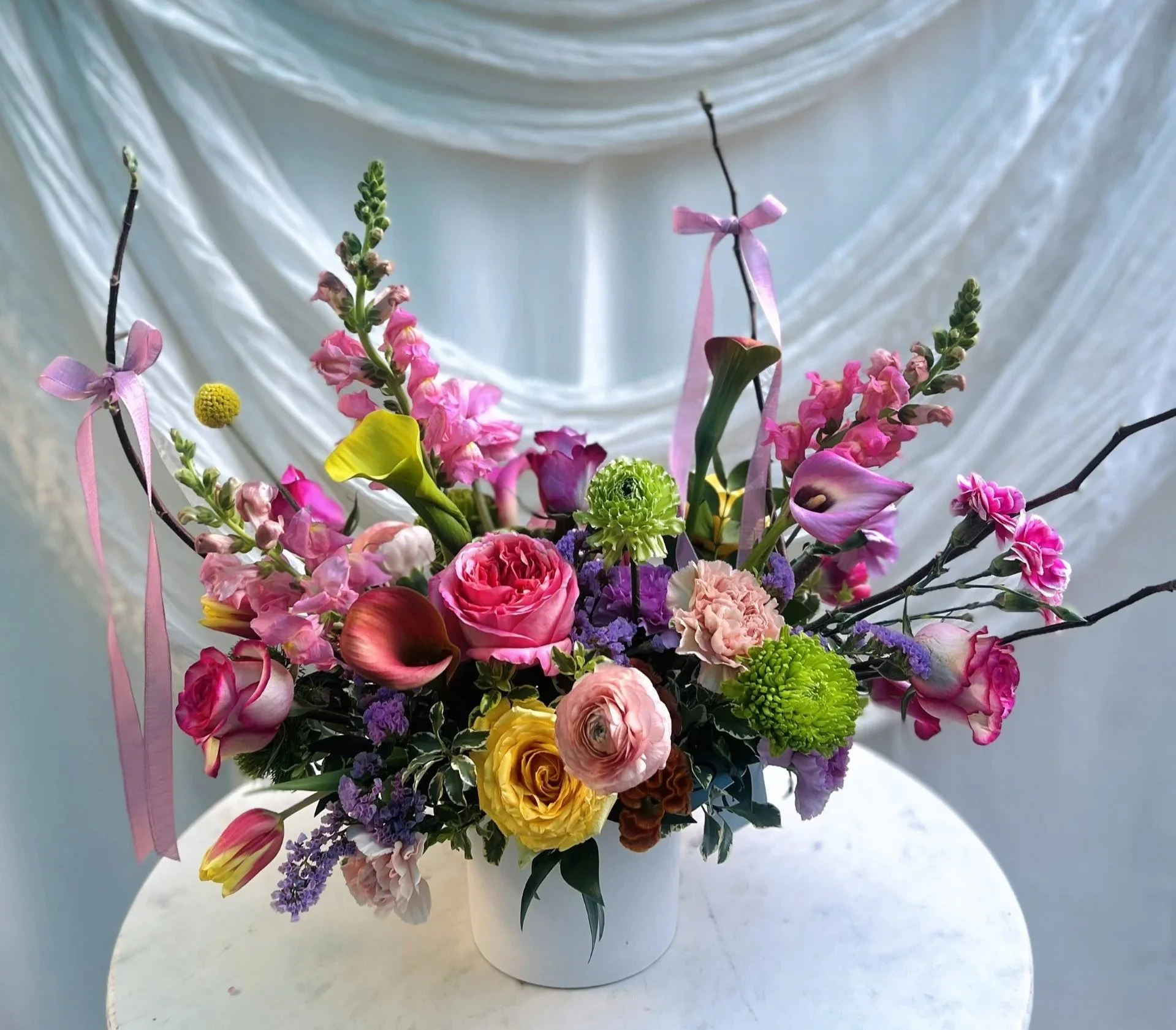 Modern vibrant floral arrangement designed in a white vase with pink, orange, and yellow with premium seasonal blooms