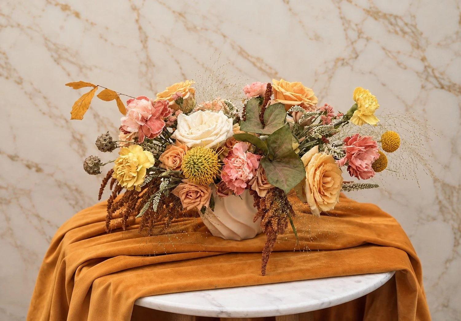Soft autumn floral arrangement with blush carnations, champagne roses, golden flowers and textural seasonal botanicals in a neutral ceramic vase.
