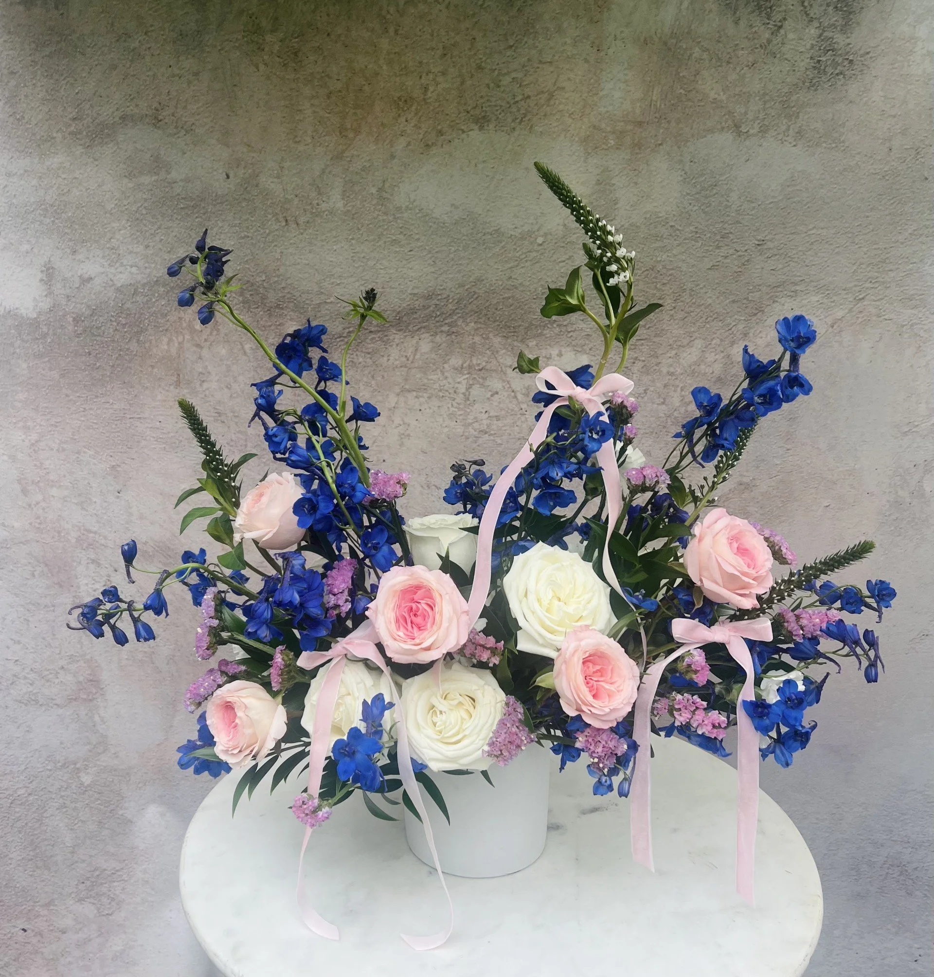 Soft pink blue and white flower arrangement featuring delphinium and garden roses with airy garden style design