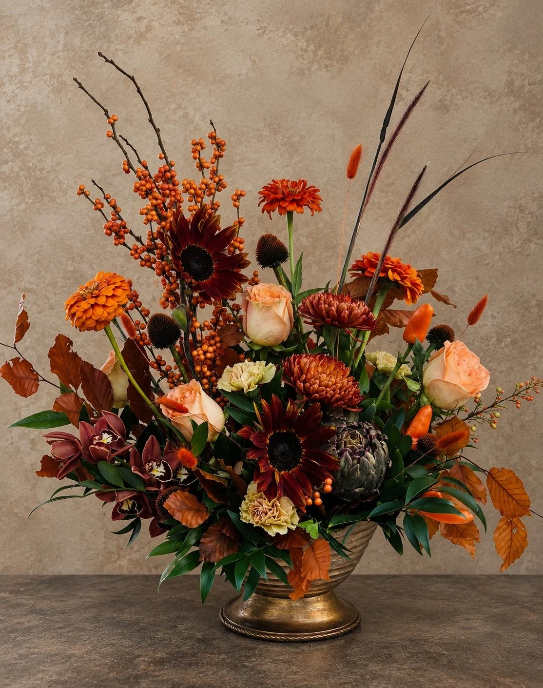 Moody autumn floral arrangement with burgundy sunflowers, peach roses, orchids, berries and sculptural fall botanicals in a vintage metallic vase.