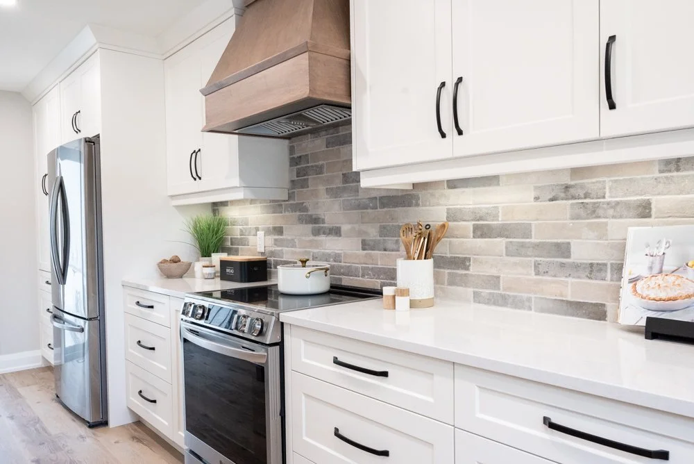 Modern kitchen with white cabinets, stainless steel refrigerator, oven, and a brick-style backsplash.