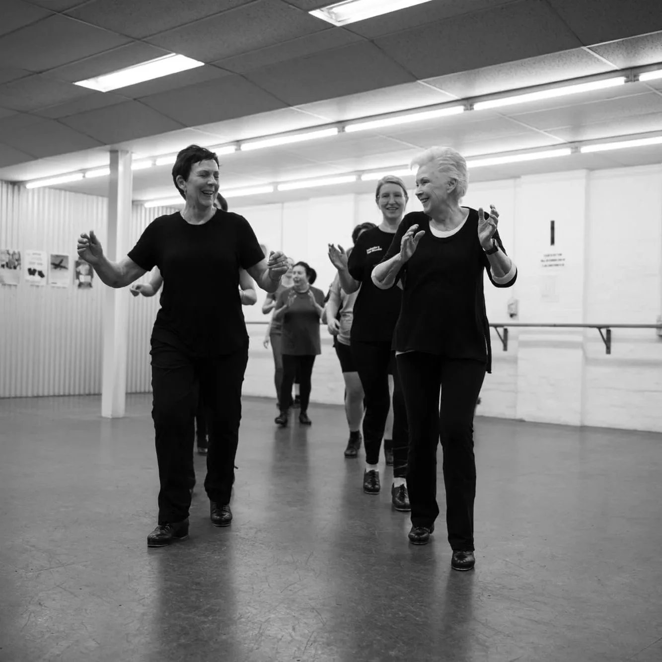 A group of women in an adult tap dance class moving across the studio dance floor