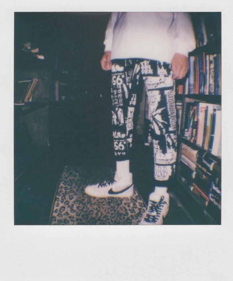 Person wearing white and black graphic pants and white sneakers, standing on a leopard-print rug in a room with bookshelves.