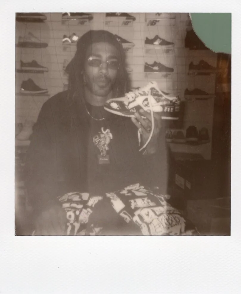 Person with glasses and shoulder-length hair holding a sneaker inside a shoe store.