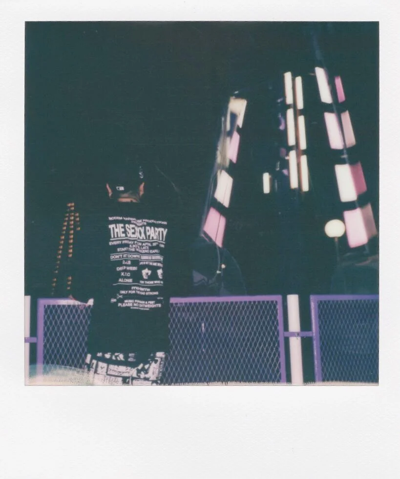 Nighttime city scene with a person standing in front of a billboard and neon-lit buildings.