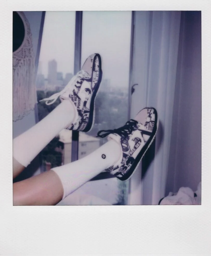 Person wearing white socks and sneakers with a cityscape view in the background, seen from a high-rise balcony.
