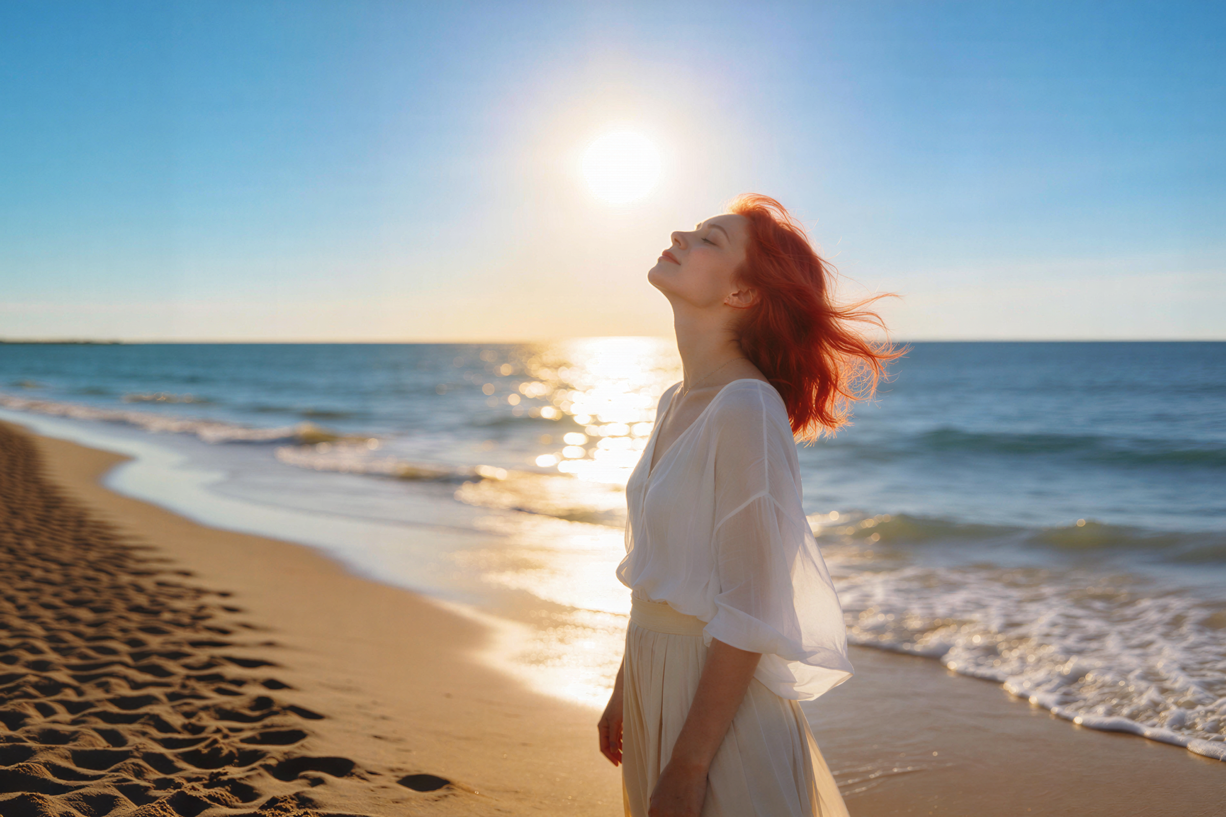 A woman with red hair in a white dress stands on a sandy beach at sunset, facing the sun with her eyes closed and head tilted back, enjoying the warm light by the ocean.