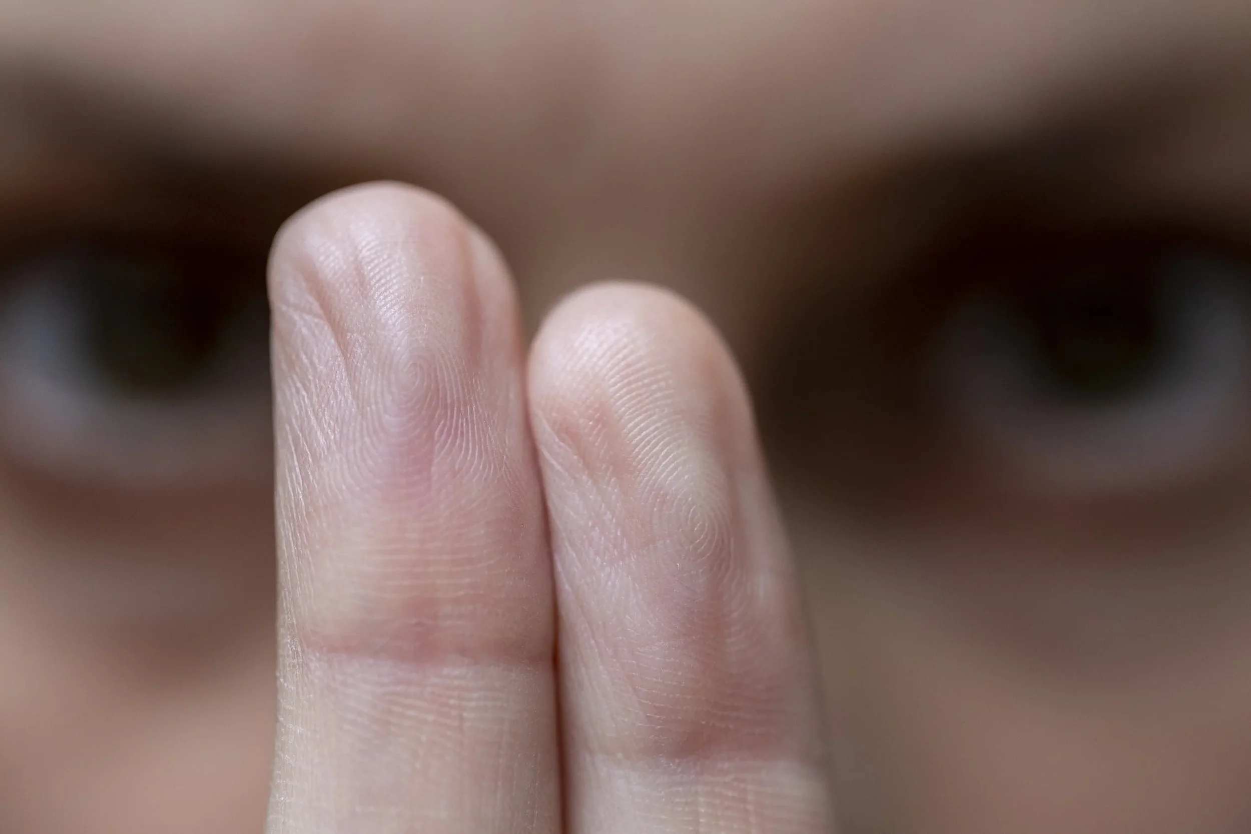 Two fingers held closely together in front of a persons face, with the face out of focus in the background and the finger details in sharp focus.