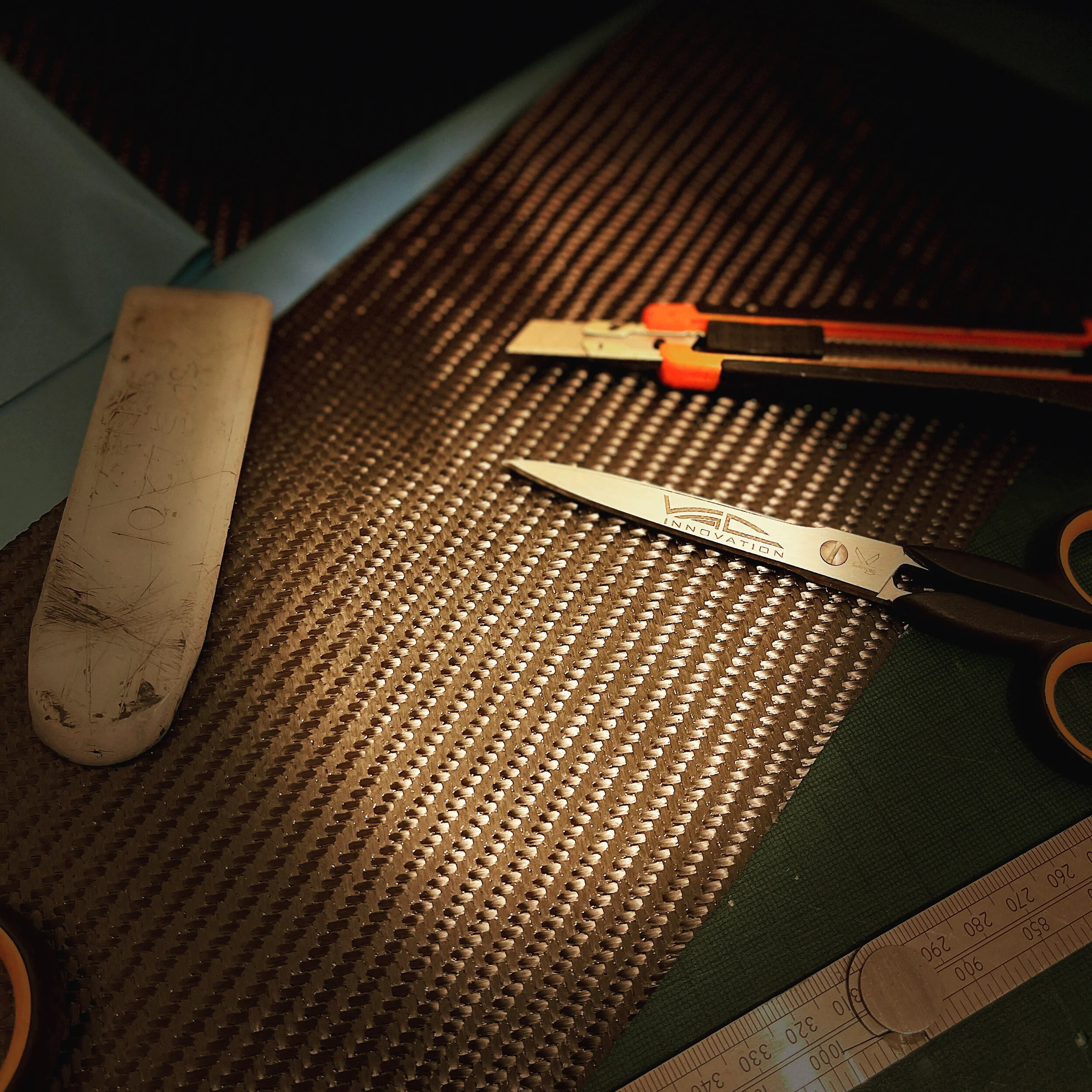 Close-up of a textured surface with a white cylindrical object, a ruler, and a pair of scissors with orange handles on top. The scene appears to involve measurement or crafting tools.