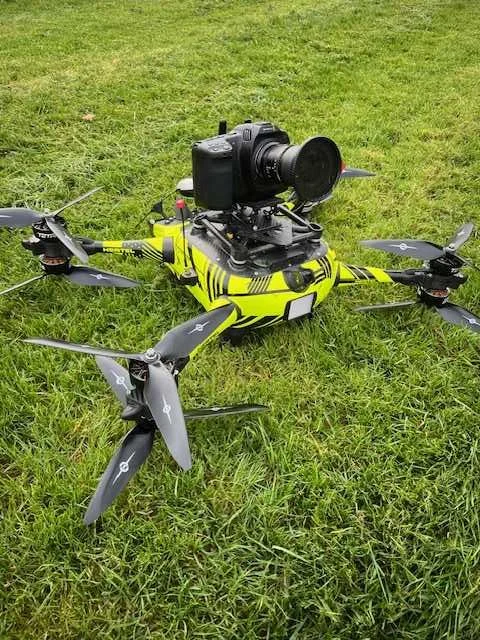 A yellow and black drone with a camera mounted on top, resting on green grass