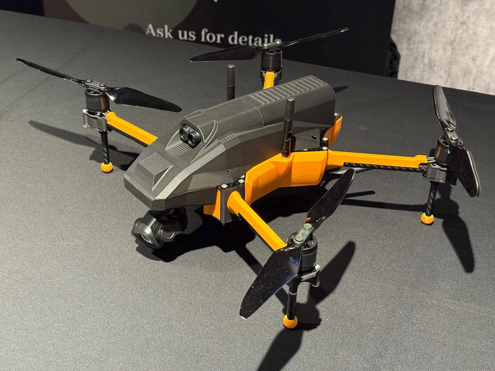 A small drone with an orange and black color scheme on a gray surface, with four propellers and mounted camera underneath.