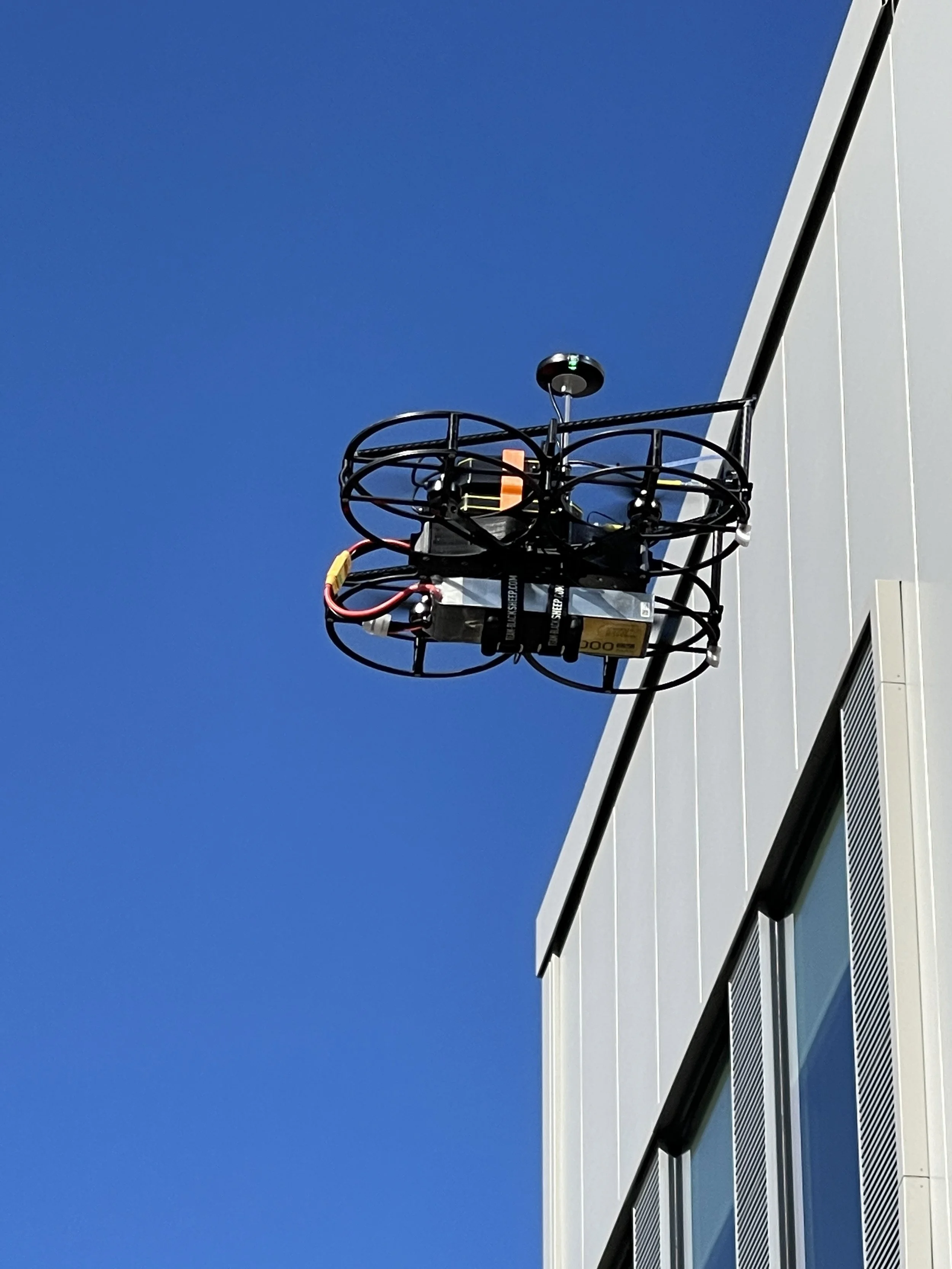 A drone is mounted on the exterior wall of a modern building under a clear blue sky.