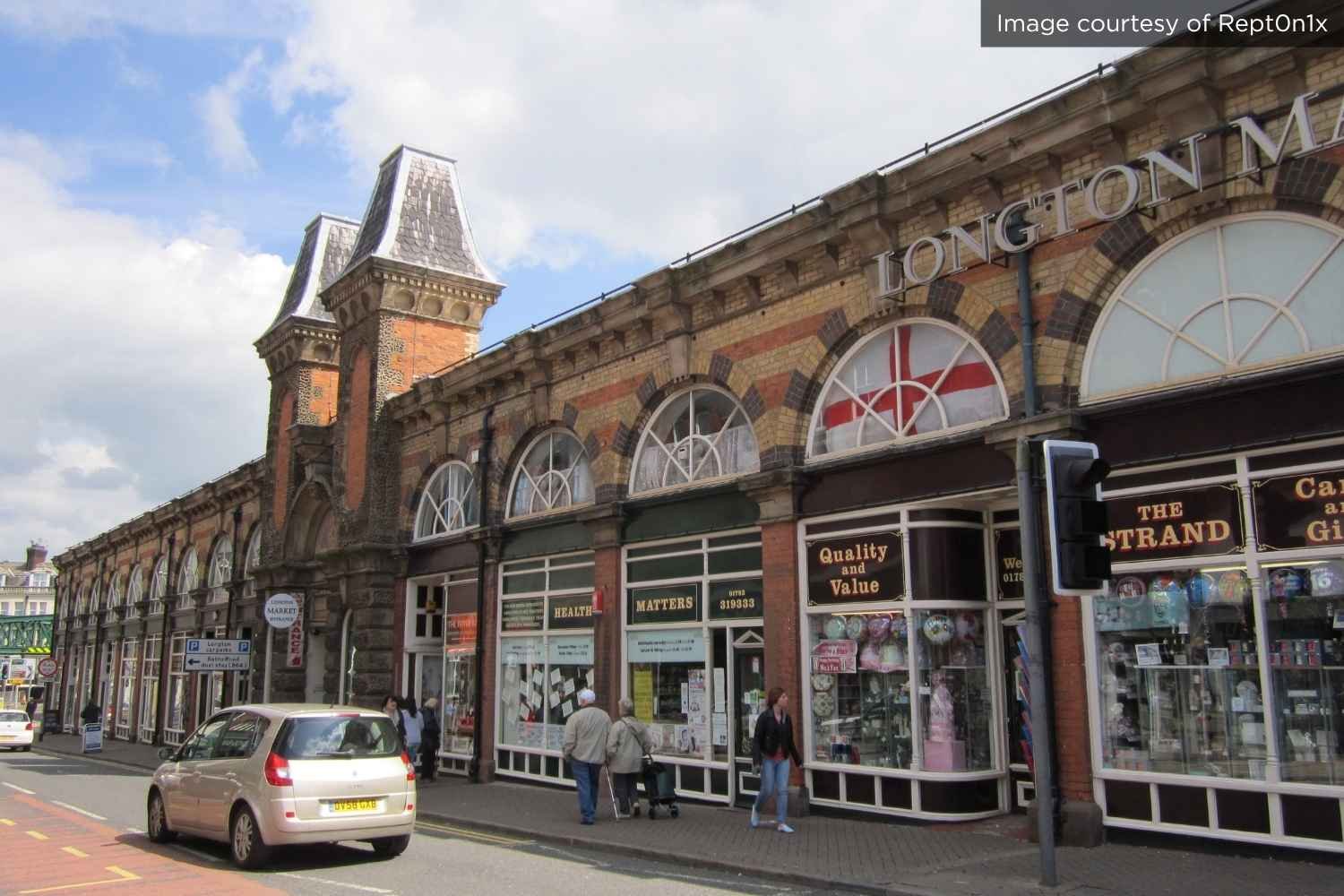 A car and pedestrians pass by shopfronts at Longton's Victorian market
