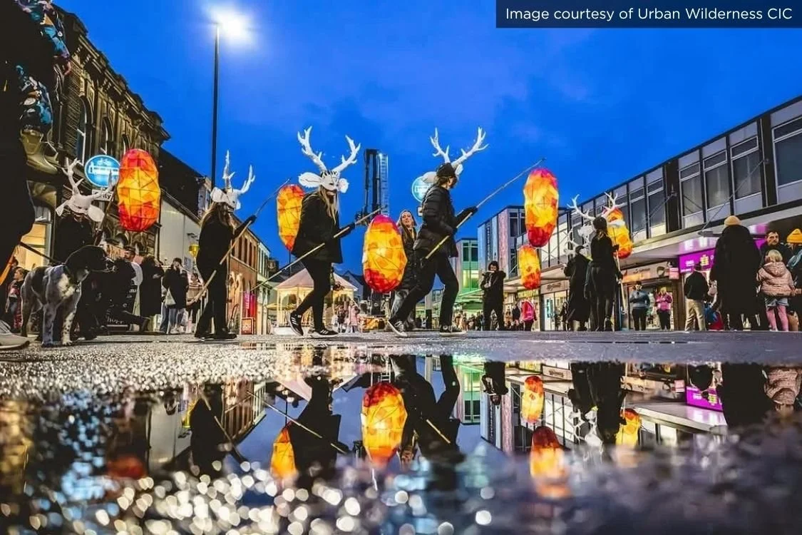 People cross the street in masks holding lanterns at Longton's fourth annual Carnival and Pig Walk Parade