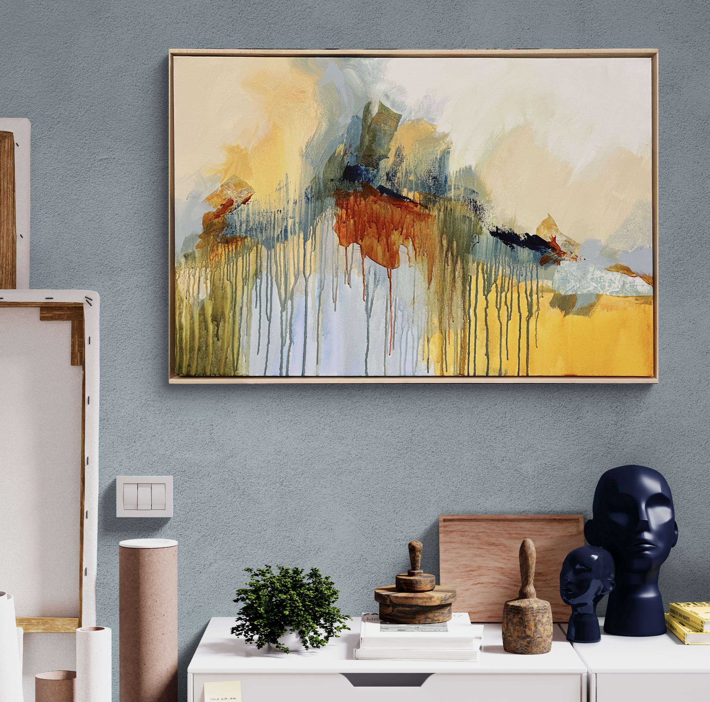 Abstract watercolor painting with drips and patches of orange, yellow, green, blue, and black, hanging on a blue wall.