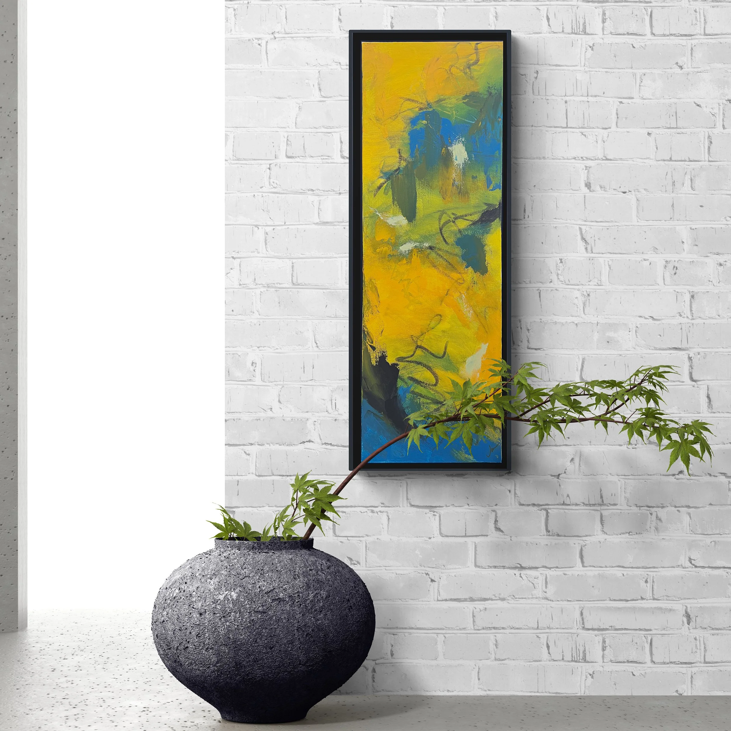 A modern interior with a white brick wall, a tall framed abstract painting with yellow, green, and blue colors, a black textured round pot with a green plant extending outward, and bright natural lighting.