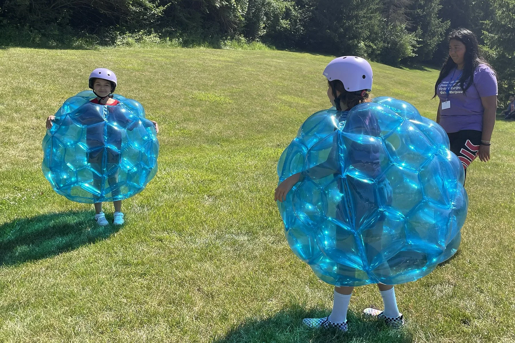 Two young girls wearing purple helmets and big blue bubble suits