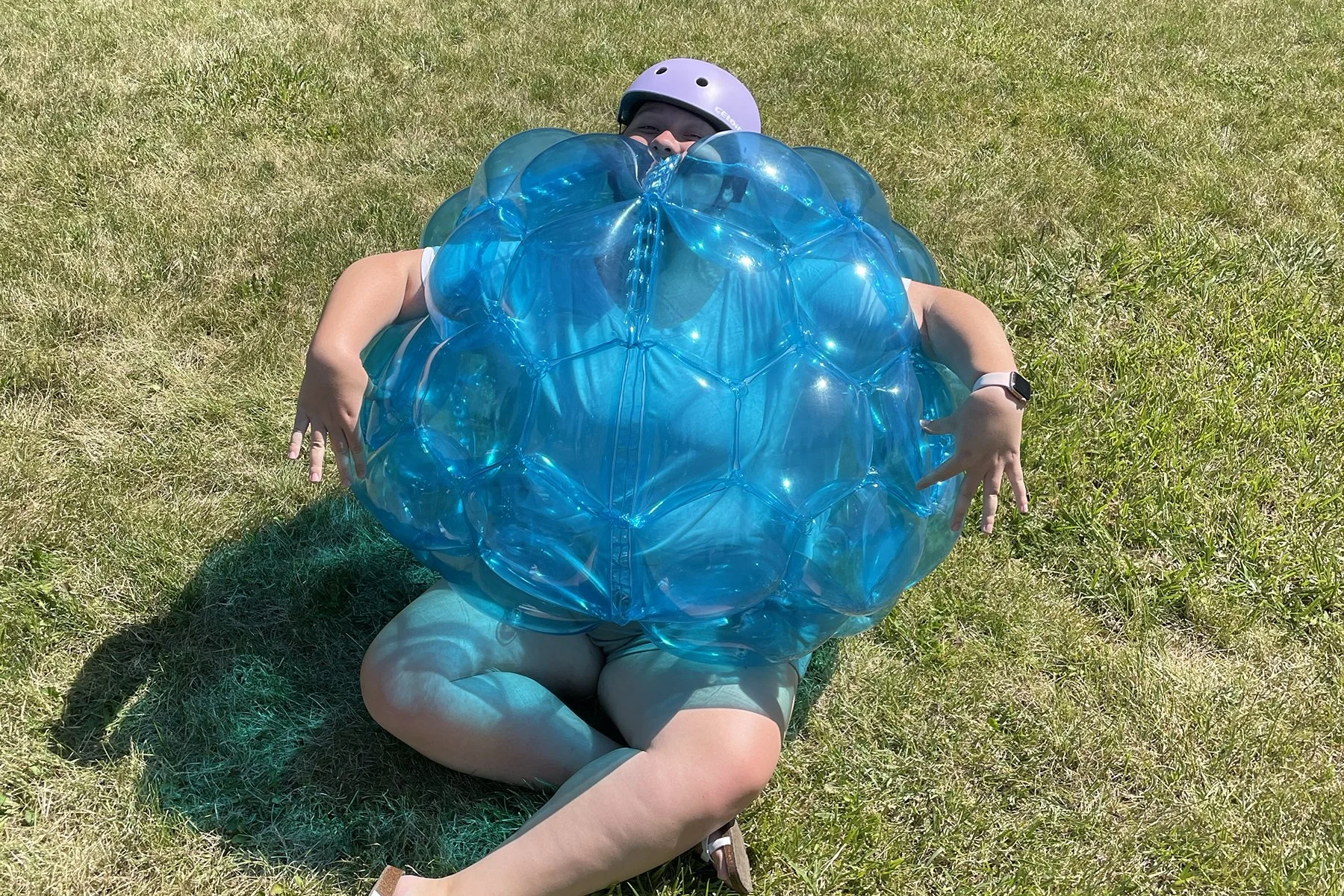 Girl sitting on the ground wearing a purple helmet and a bit blue bubble suit