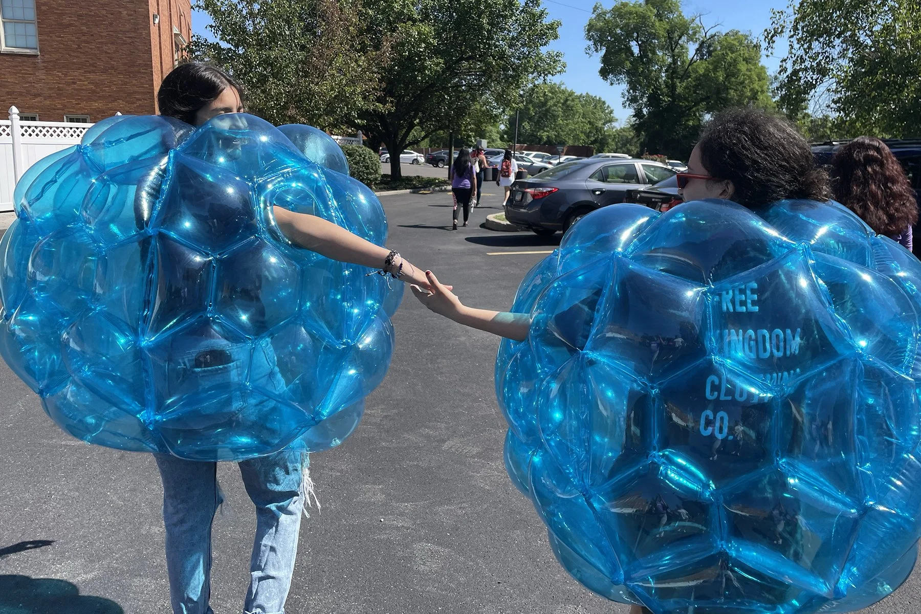 Two girls walking hand in hand wear big blue bubble suits