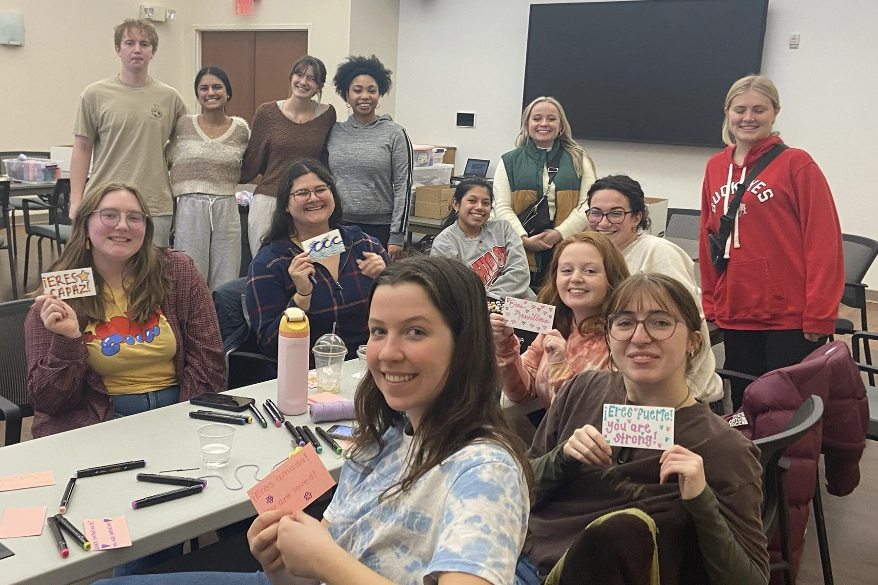 Group of women and men sitting at a table writing uplifting messages on index cards