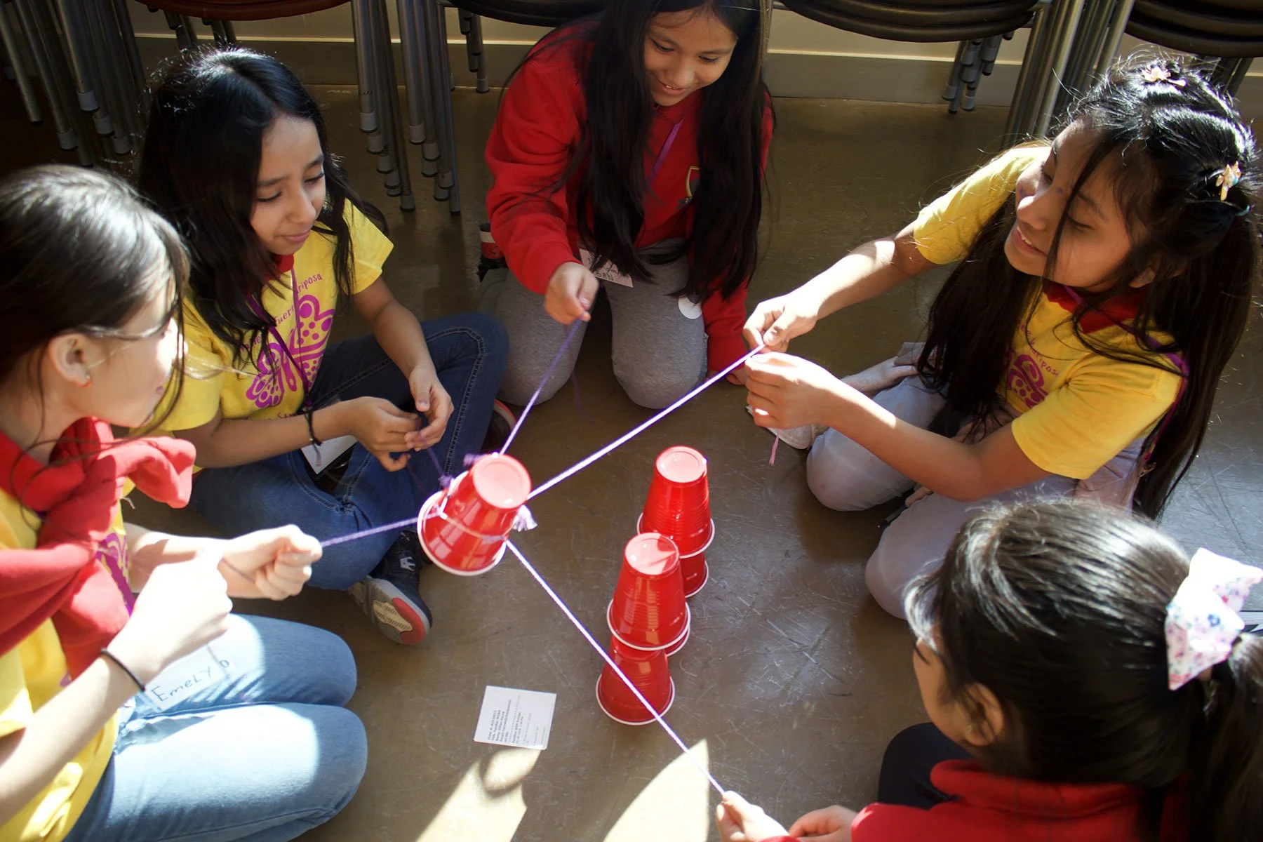 Group of girls working together to move a cup using pieces of string